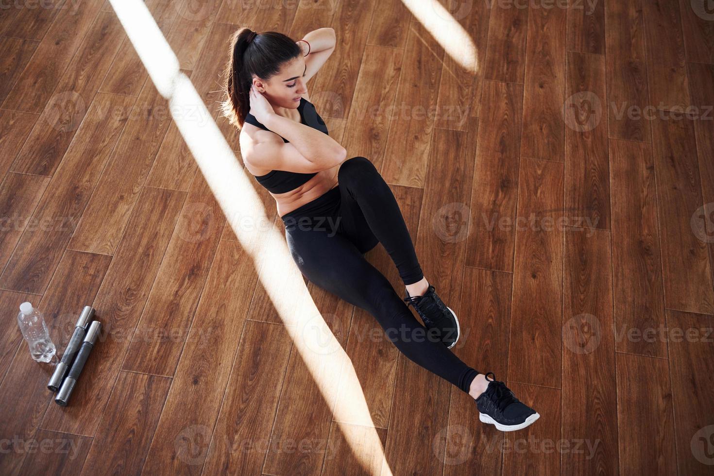 auf dem von Lichtstrahlen beleuchteten Boden. junge sportliche frau in sportbekleidung, die fitness im fitnessstudio macht foto