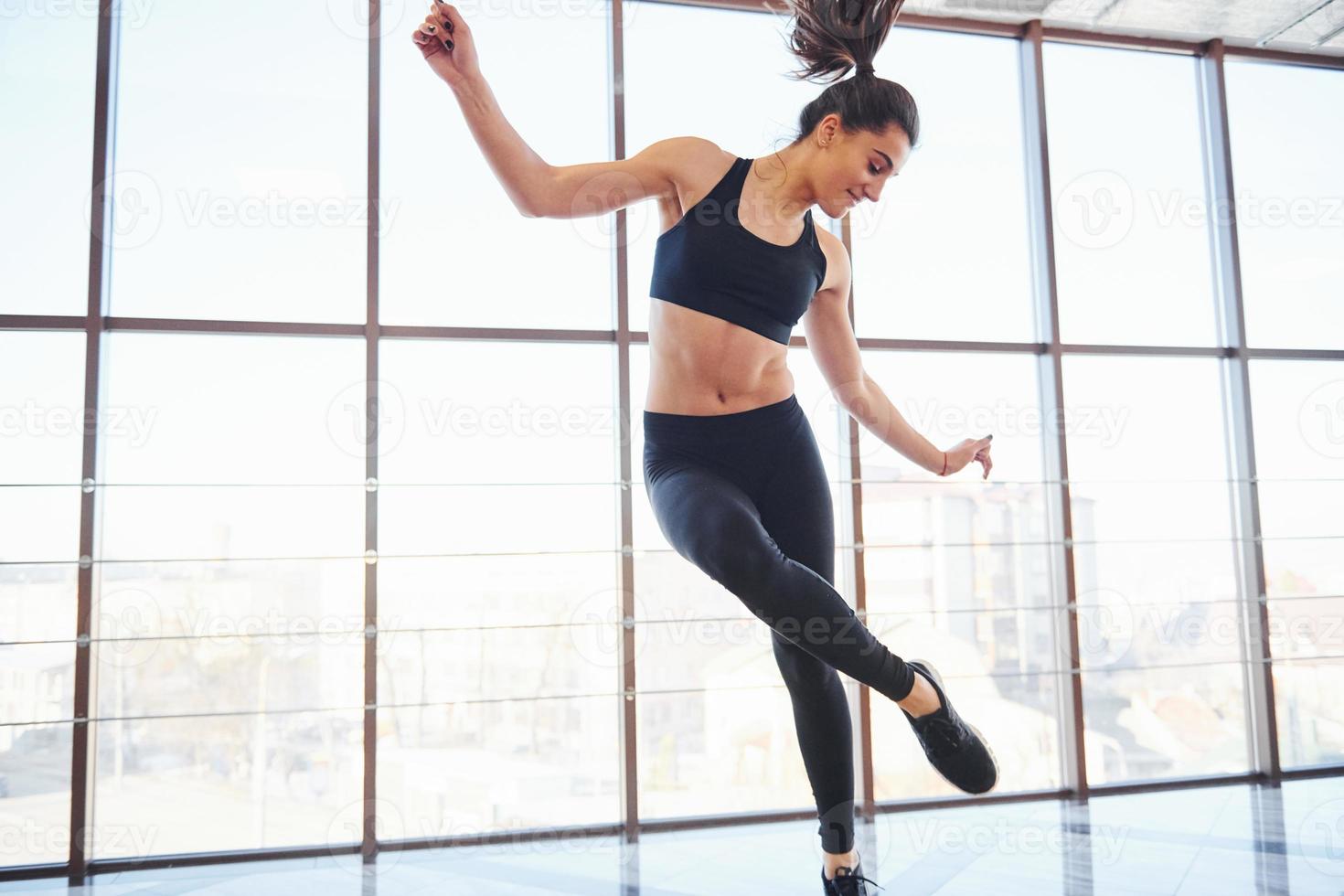 Junge sportliche Frau in Sportbekleidung, die sportliche Tricks gegen das Fenster macht foto