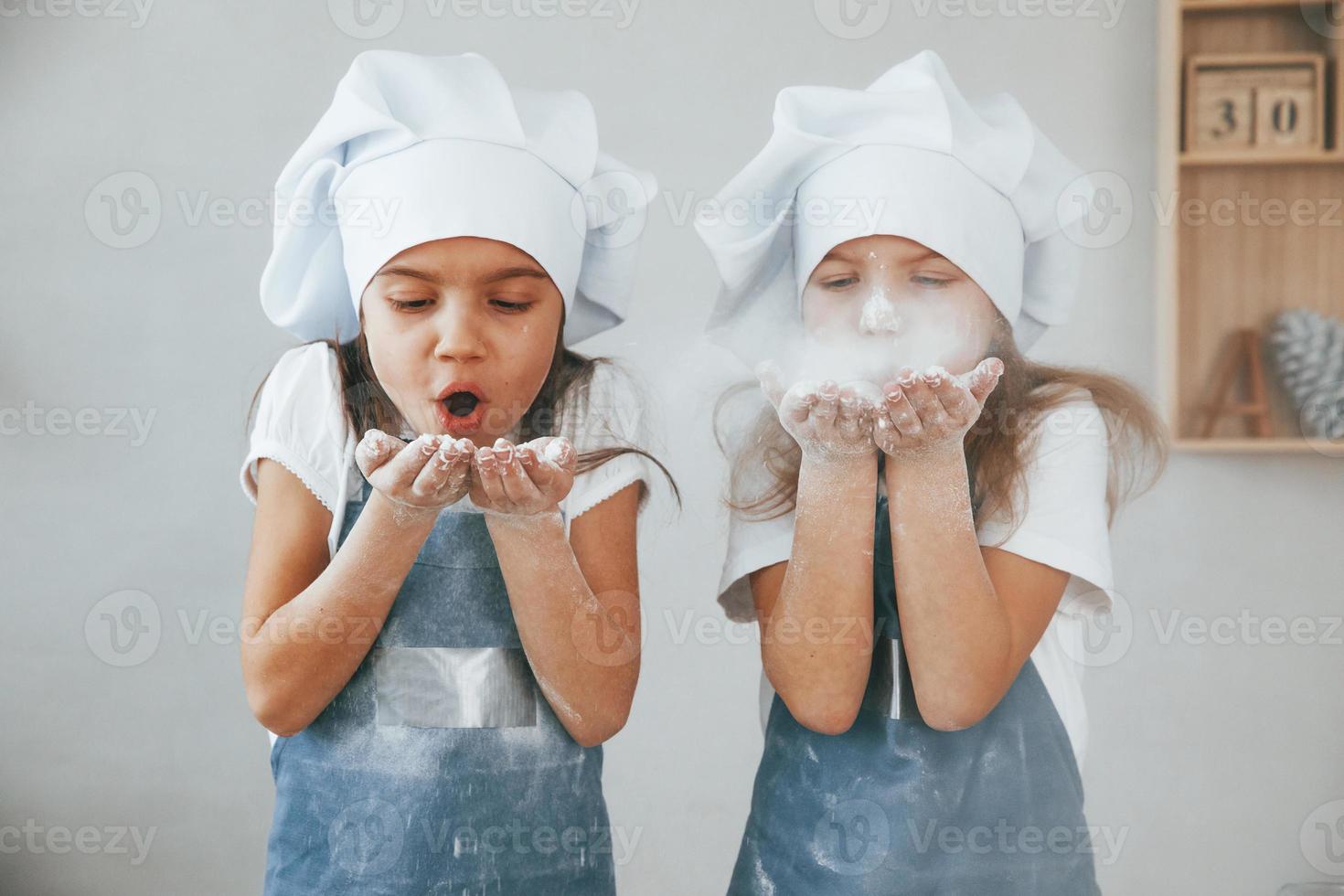 zwei kleine mädchen in blauer kochuniform blasen das mehl in der küche aus den händen foto