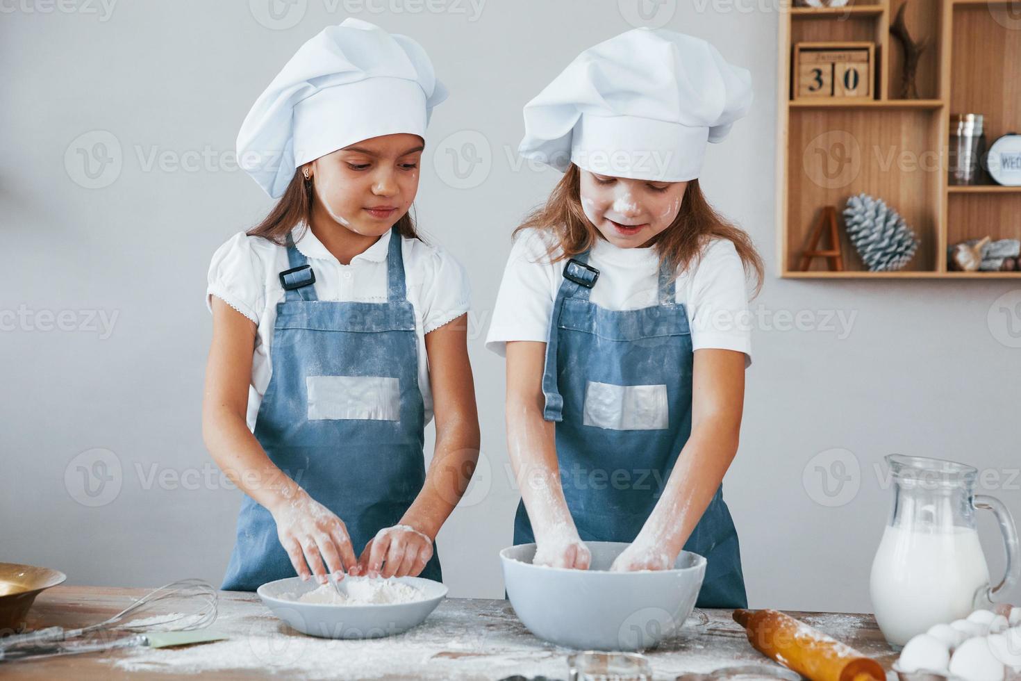 Zwei kleine Mädchen in blauer Kochuniform arbeiten mit Mehl in der Küche foto