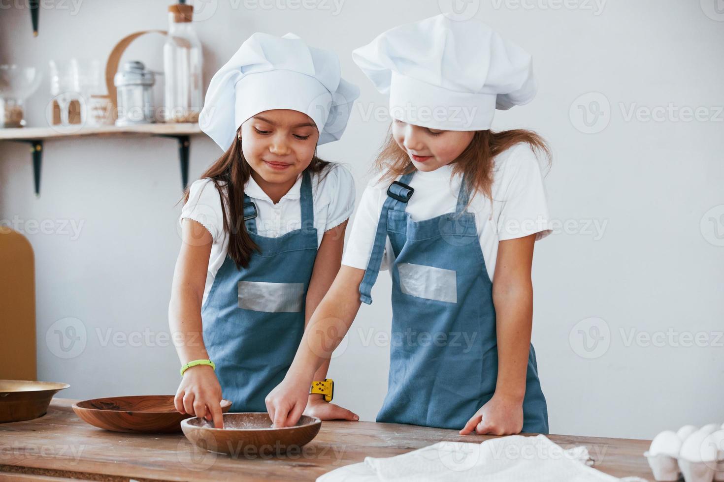 Zwei kleine Mädchen in blauer Kochuniform arbeiten mit Mehl in der Küche foto