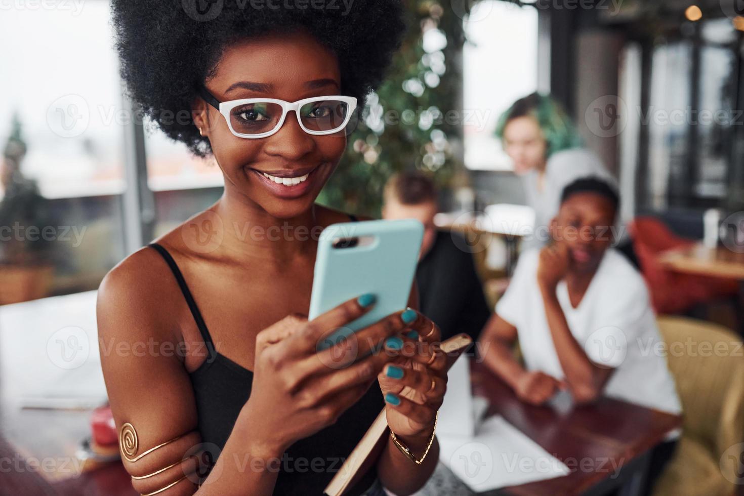 Schwarze Frau, die vor einer Gruppe multiethnischer Menschen mit alternativen Mädchen mit grünen Haaren steht, arbeitet drinnen am Tisch zusammen foto