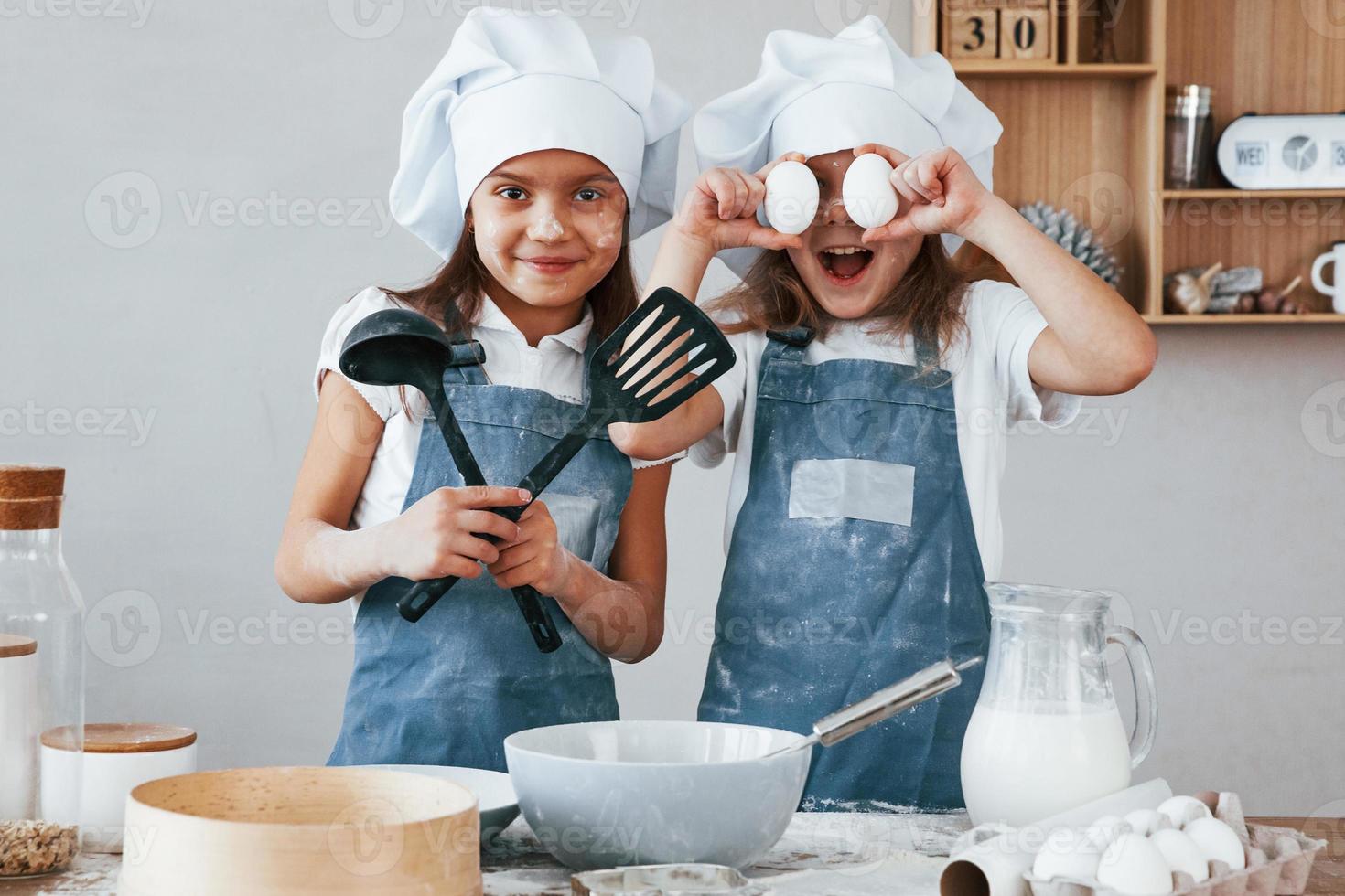 Zwei kleine Mädchen in blauer Kochuniform haben Spaß beim Zubereiten von Speisen in der Küche foto