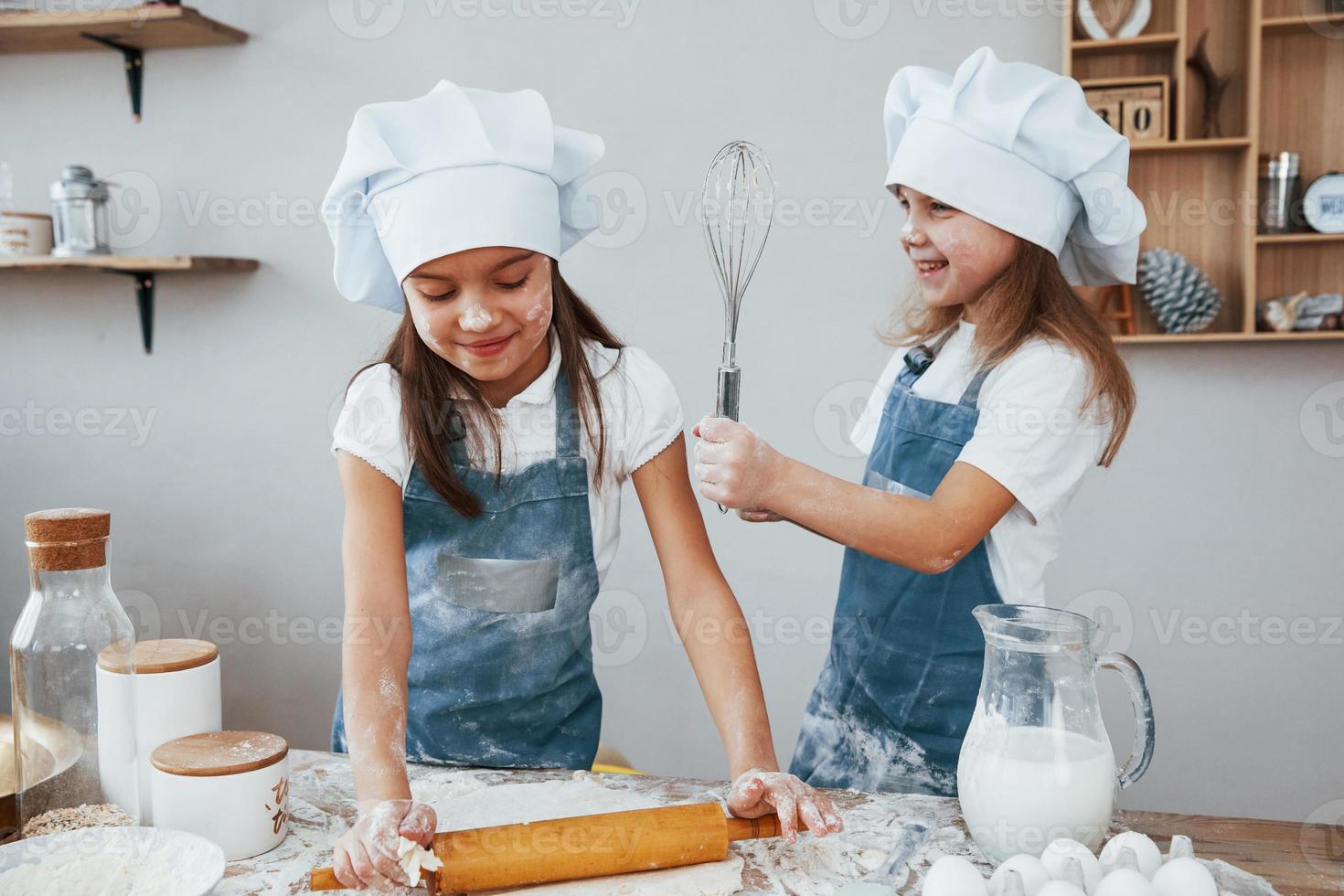 Zwei kleine Mädchen in blauer Kochuniform kneten Teig in der Küche foto