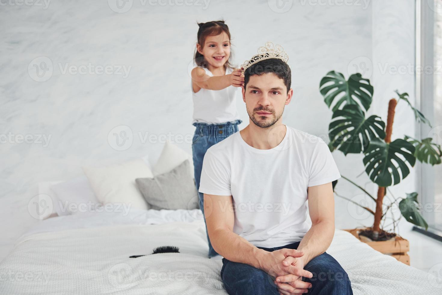 kleines Mädchen mit Krone auf dem Kopf des Vaters. zusammen Spaß zu Hause haben foto
