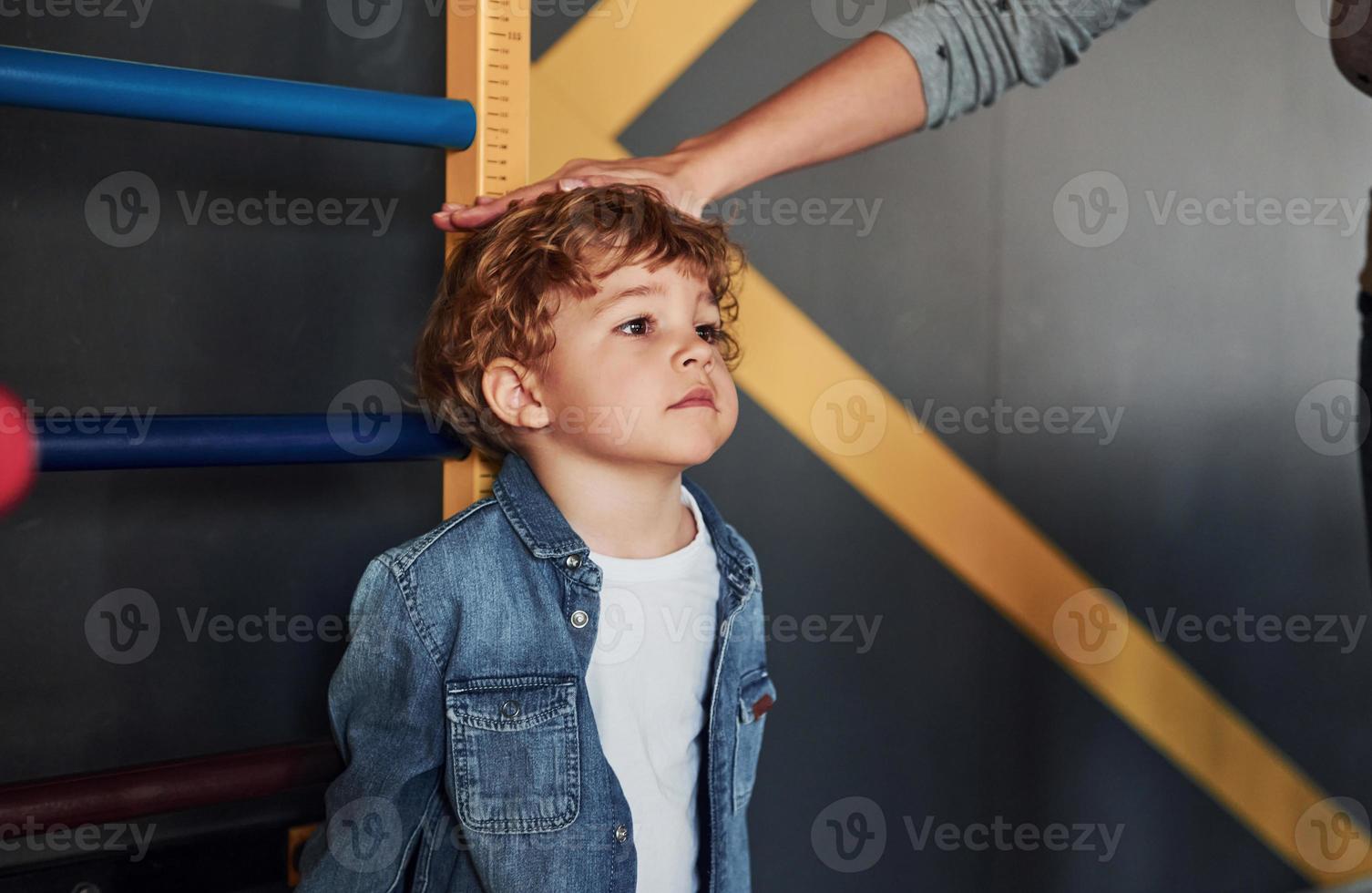 lehrer, der die größe des kindes drinnen im kindergarten misst foto