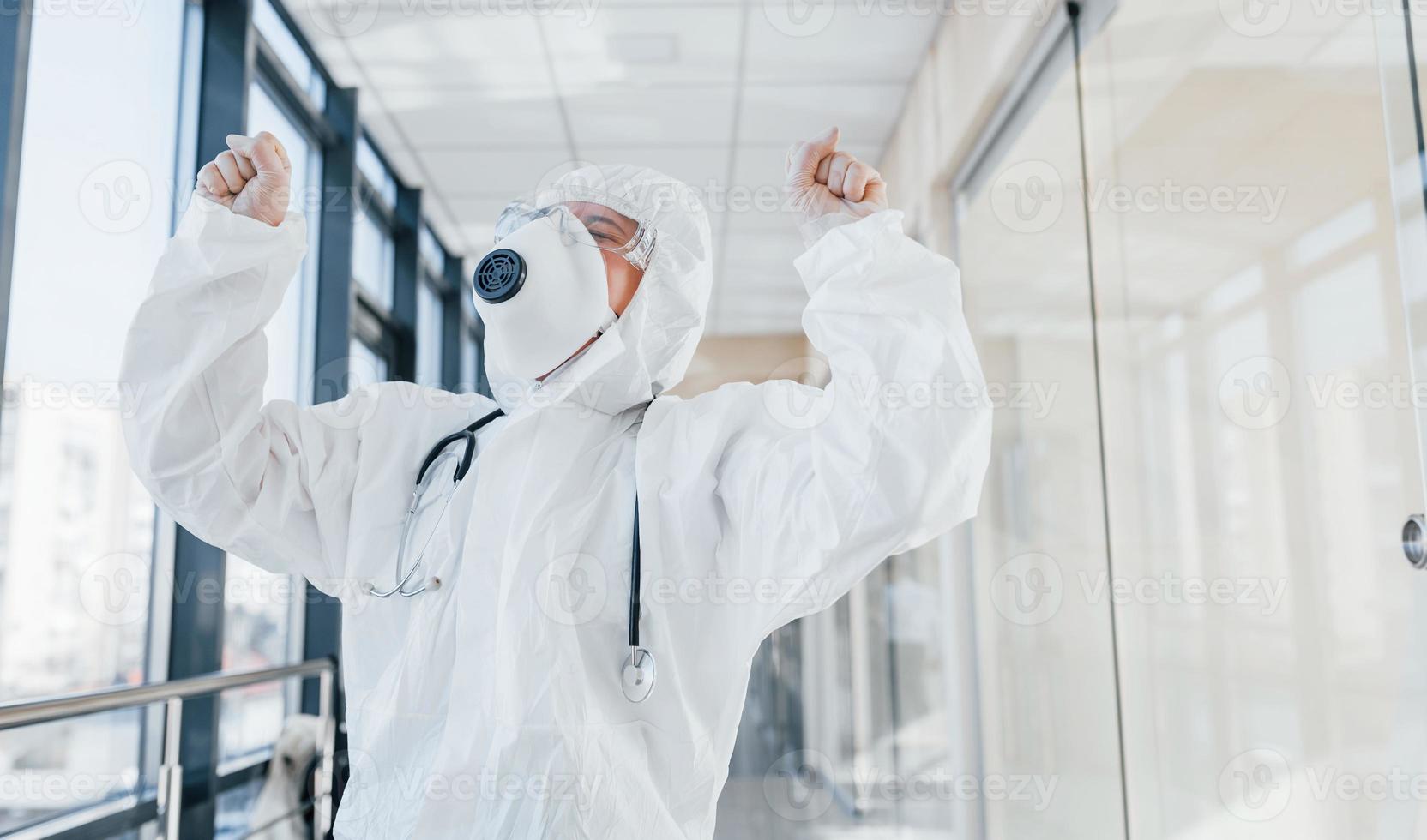 Sieg feiern. Ärztin in Laborkittel, Schutzbrille und Maske im Innenbereich foto