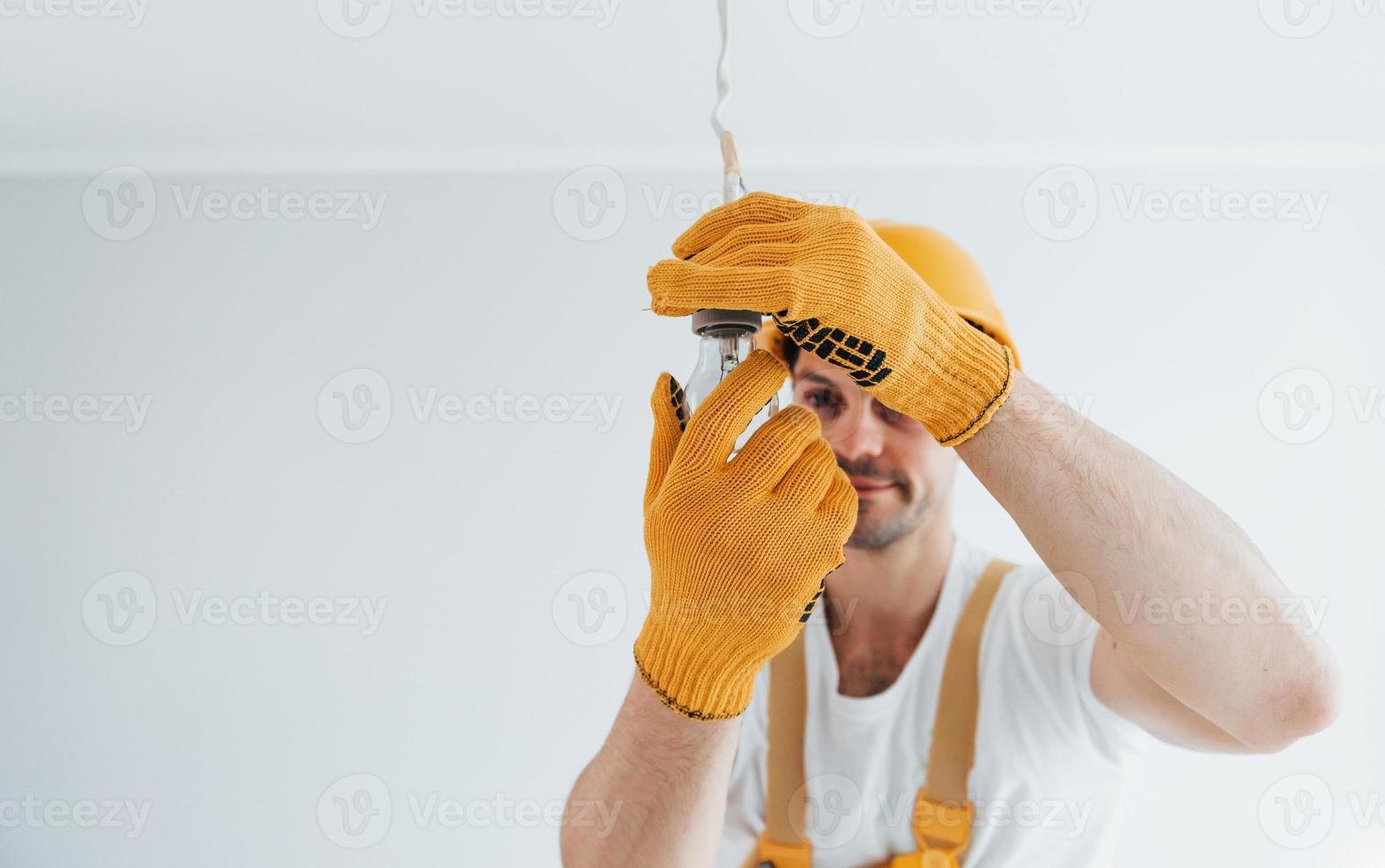 handwerker in gelber uniform wechselnder glühbirne. haussanierungskonzept foto