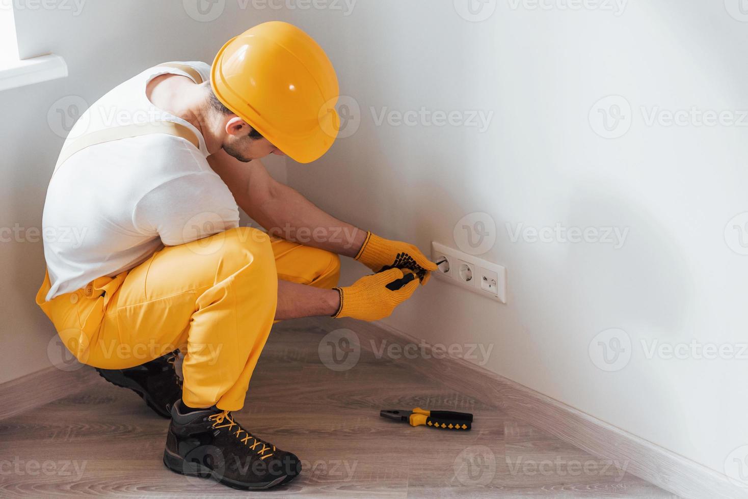 handwerker in gelber uniform arbeitet mit strom und installiert neue steckdose. haussanierungskonzept foto