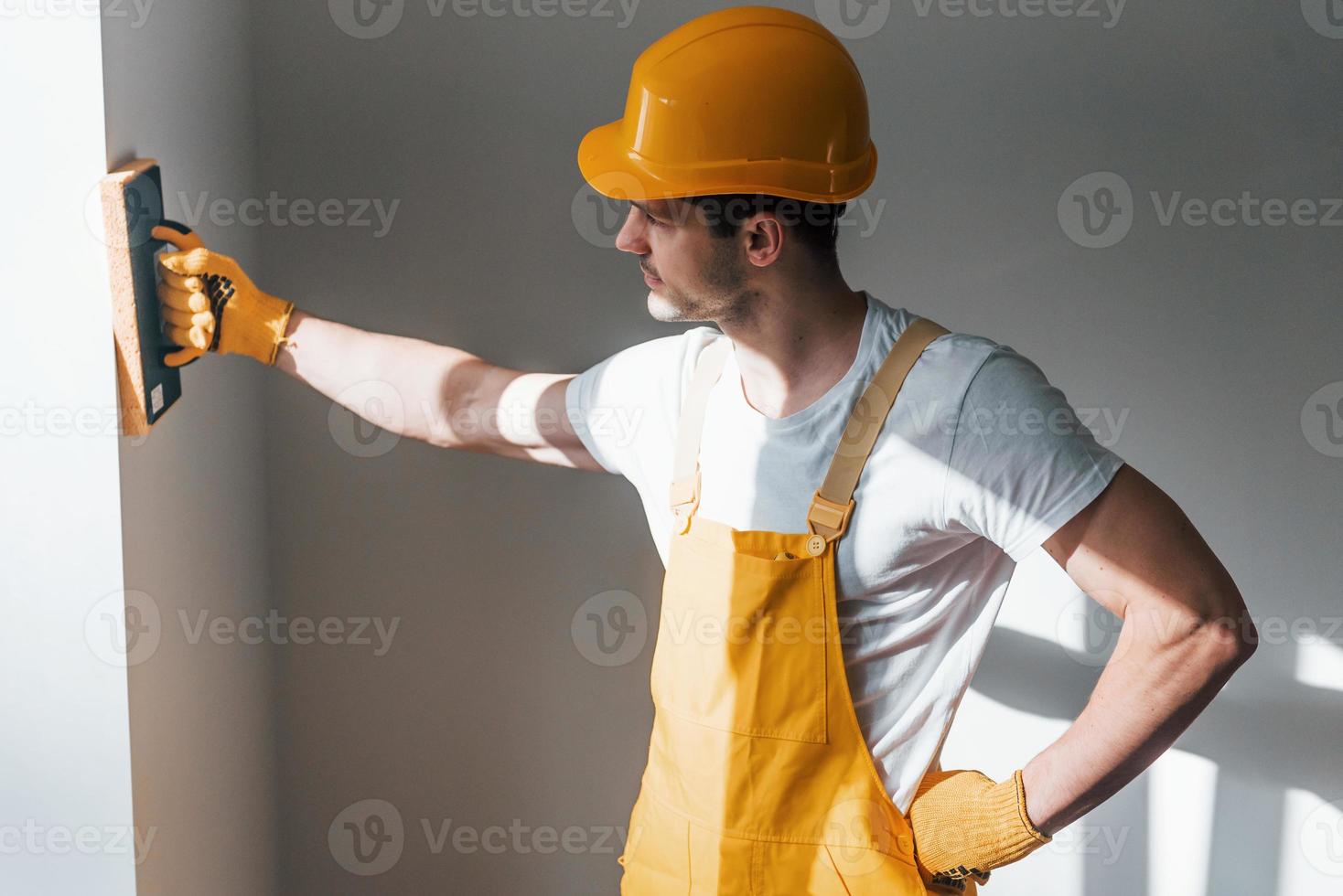 Handwerker in gelber Uniform Polierwand drinnen. haussanierungskonzept foto