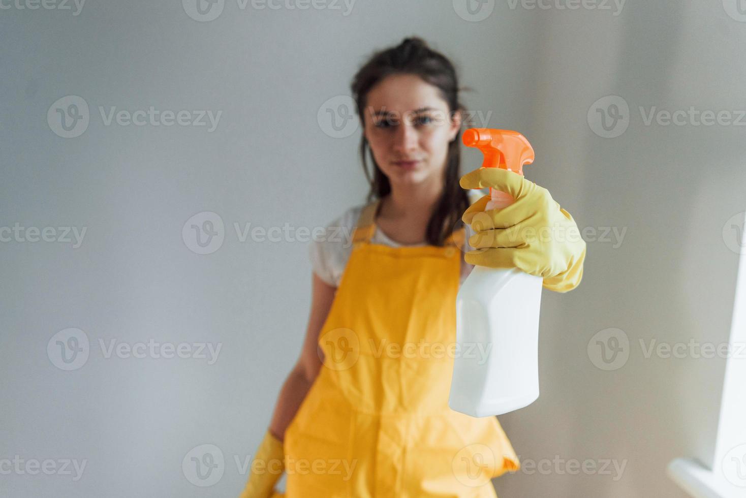 Hausfrau in gelber Uniform steht mit Reinigungsspray für Fenster im Innenbereich. haussanierungskonzept foto