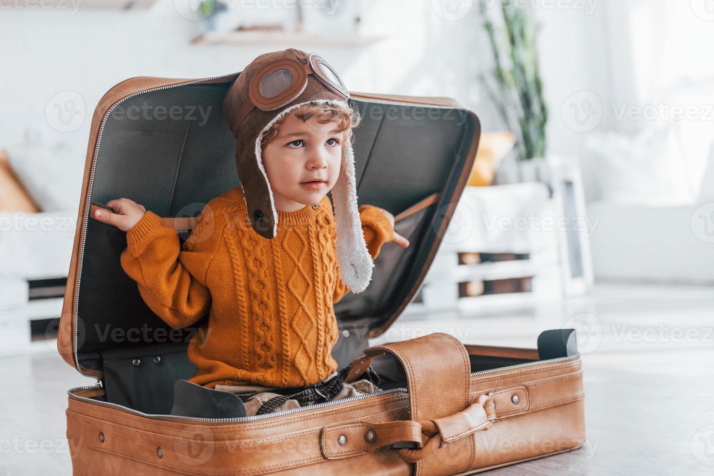 kleine jungen im retro-pilotenkostüm haben spaß und sitzen tagsüber im koffer drinnen foto