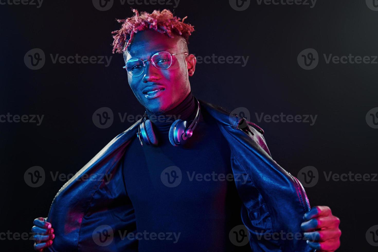 stylische Brille und kabellose Kopfhörer. futuristische neonbeleuchtung. junger Afroamerikaner im Studio foto