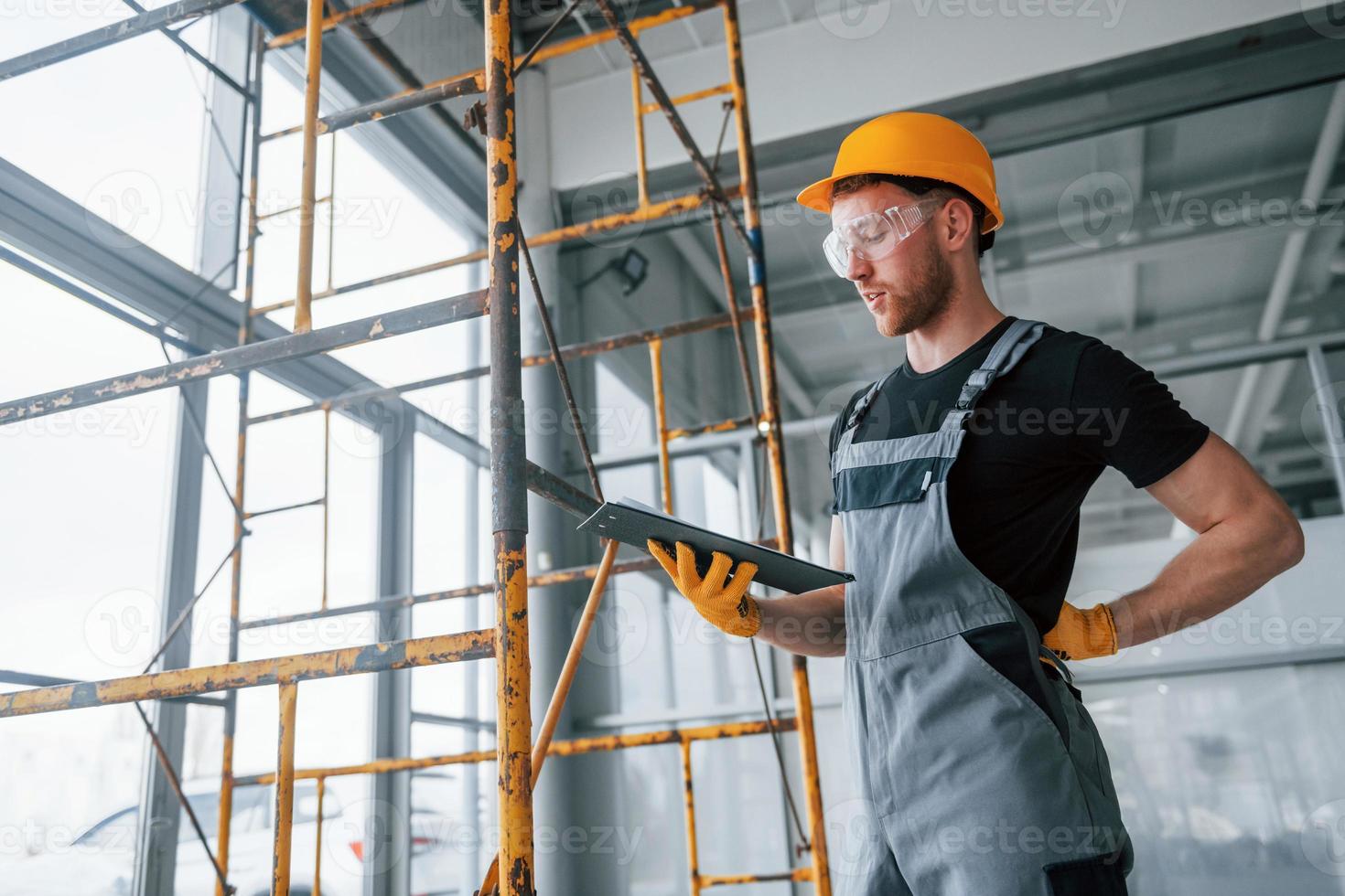 ingenieur in grauer uniform mit notizblock in den händen arbeitet tagsüber drinnen in einem modernen großen büro foto