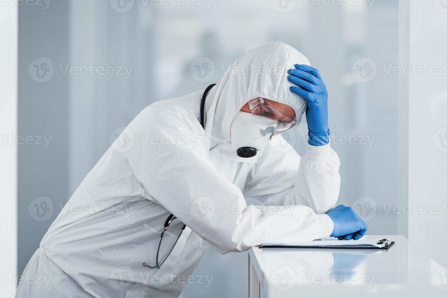 müder arztwissenschaftler in laborkittel, defensiver brille und maske macht pause foto