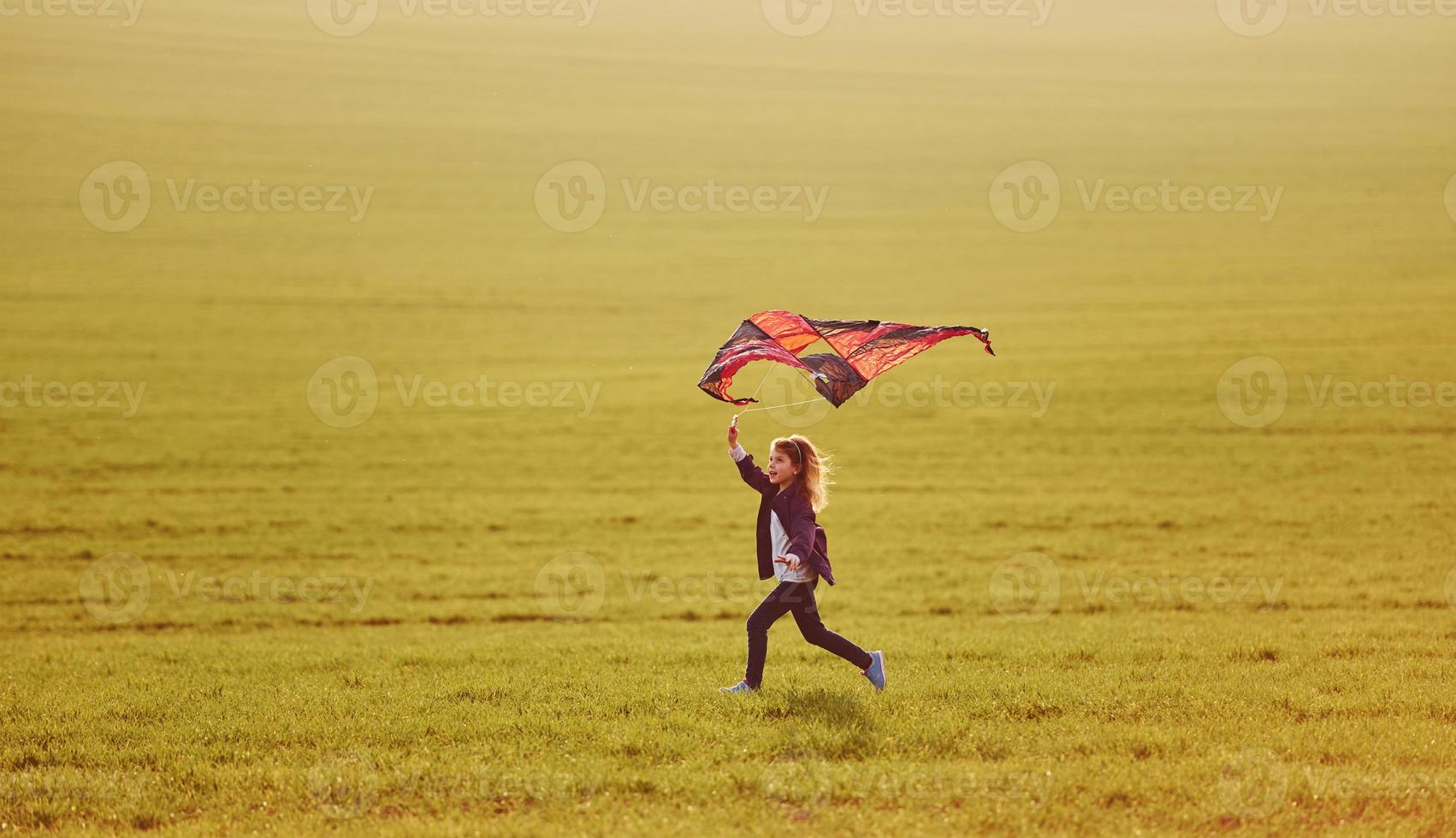 glückliches kleines mädchen, das mit drachen in den händen auf dem schönen feld läuft foto