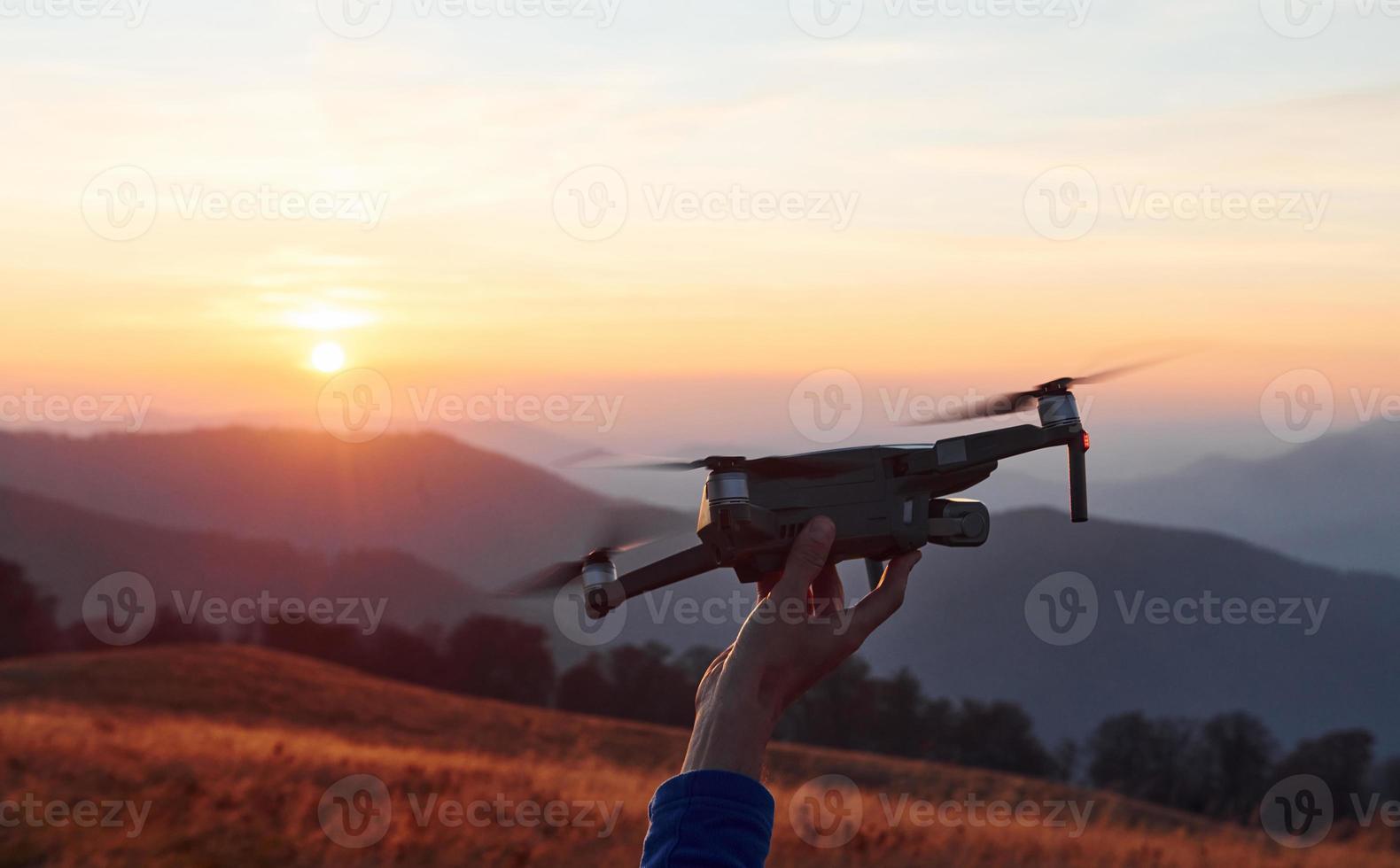 Mann steht im Herbstfeld und hält Drohne in der Hand. schöner Sonnenaufgang. majestätische Berglandschaft in der Ferne foto