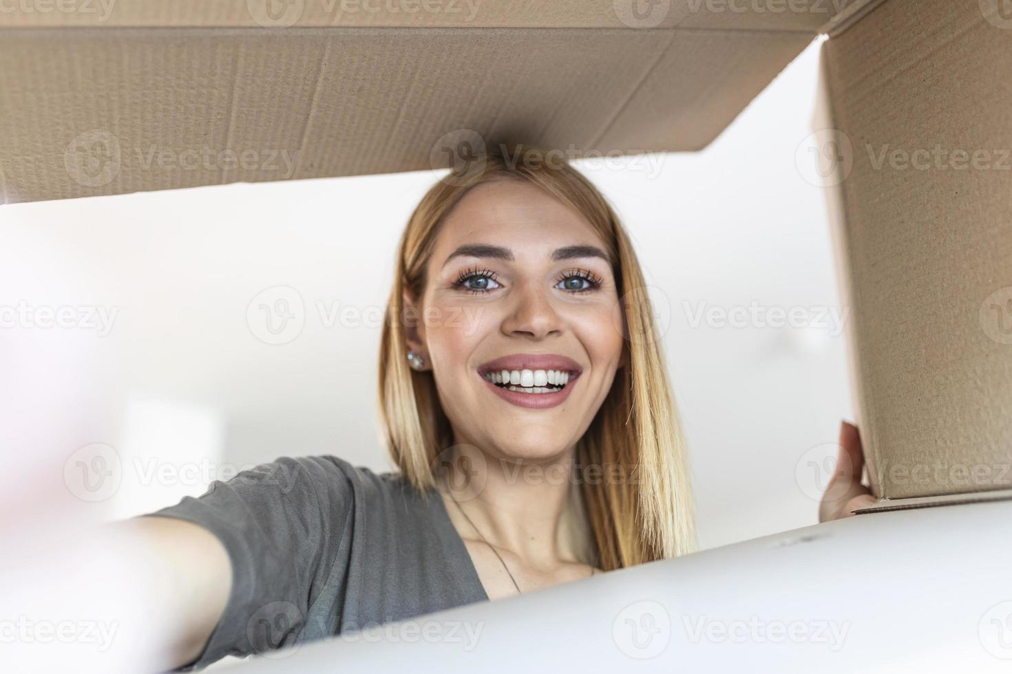 hübsche junge glückliche frau, die einen karton öffnet. Frau, die überrascht in ein Weihnachtsgeschenk schaut, während sie die Schachtel öffnet. foto