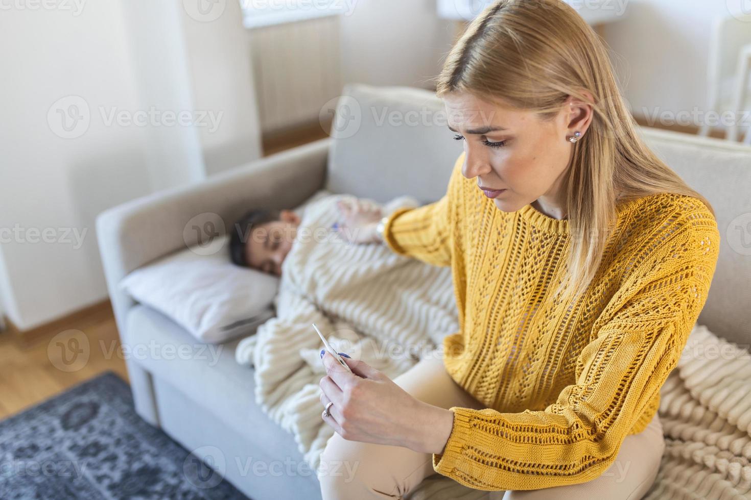 junge mutter, die den kopf des sohnes berührt, misst temperatur, erkältung oder grippe, fieber der krankheit, blick auf thermometer, husten und halsschmerzen, kleines kind, mütterpflege foto