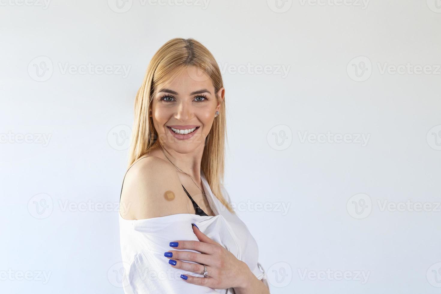 junge blonde frau, die gegen covid-19 mit einem lächeln im gesicht geimpft wurde, zeigt die impfstoffmarke foto
