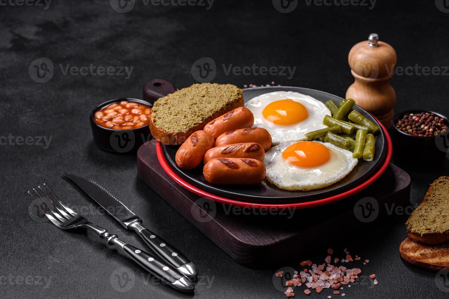 Leckeres englisches Frühstück mit Spiegeleiern, Bohnen, Spargel, Würstchen mit Gewürzen und Kräutern foto