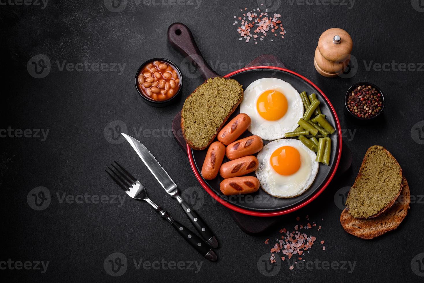 Leckeres englisches Frühstück mit Spiegeleiern, Bohnen, Spargel, Würstchen mit Gewürzen und Kräutern foto