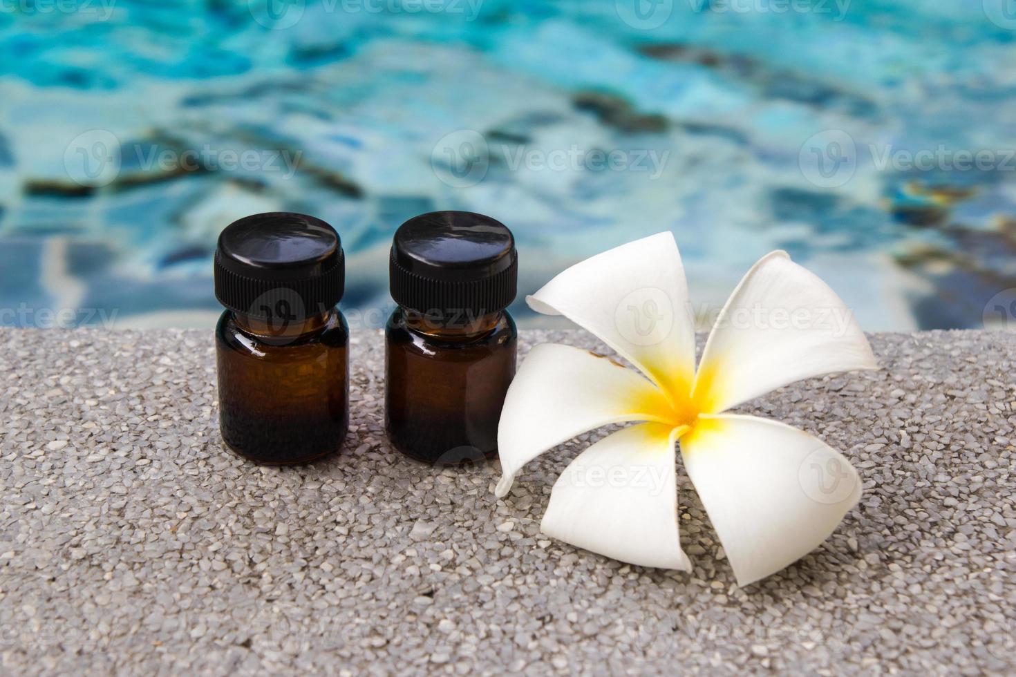 Zwei Flaschen ätherisches Aromaöl und Frangipani-Blume auf dem Swimmingpool-Hintergrund für das Spa-Thema. foto
