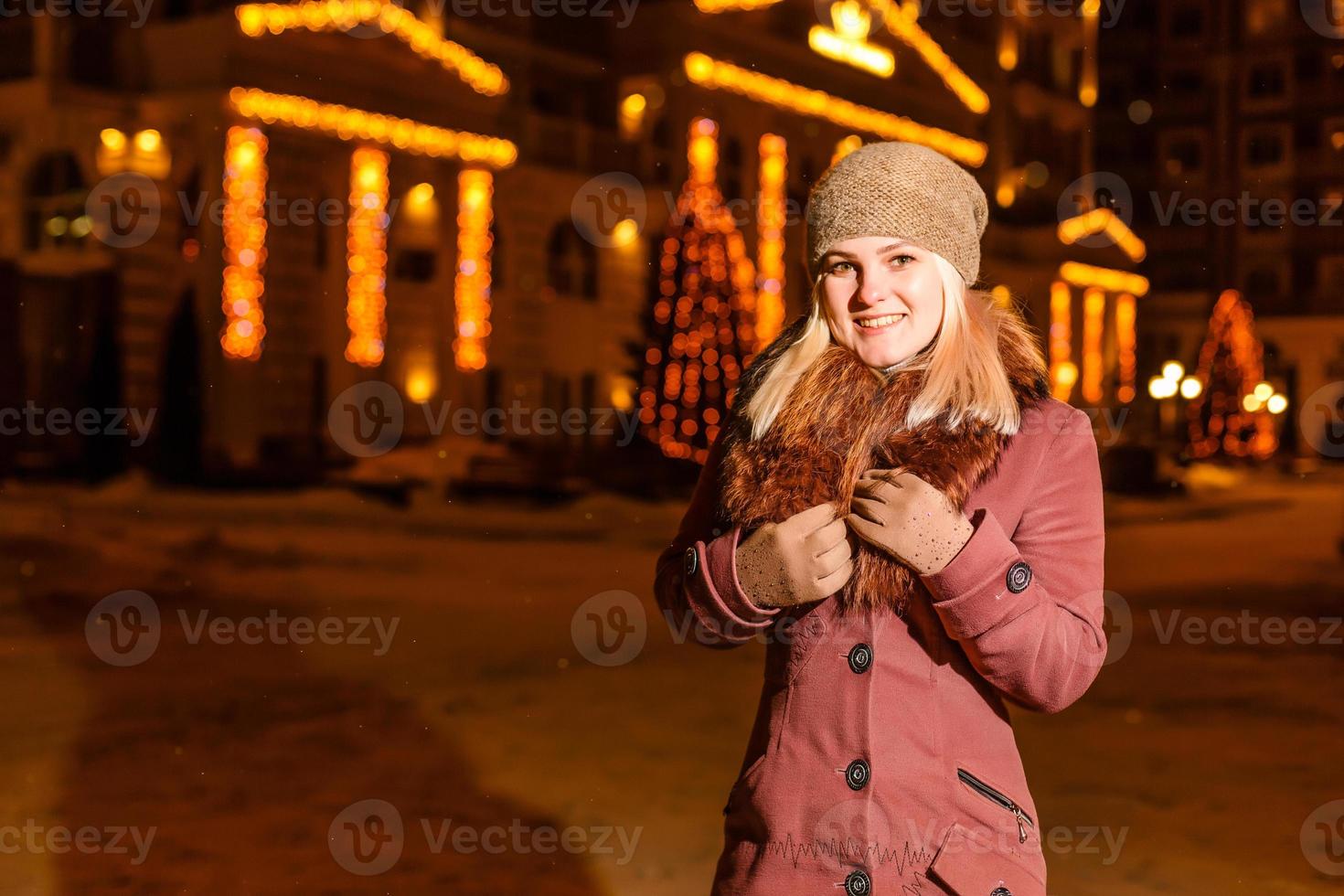 Straßenporträt einer lächelnden schönen jungen Frau auf dem festlichen Weihnachtsmarkt. dame, die klassische, stilvolle winterstrickkleidung trägt. modell, das kamera betrachtet. magischer Schneefall-Effekt. Nahansicht foto