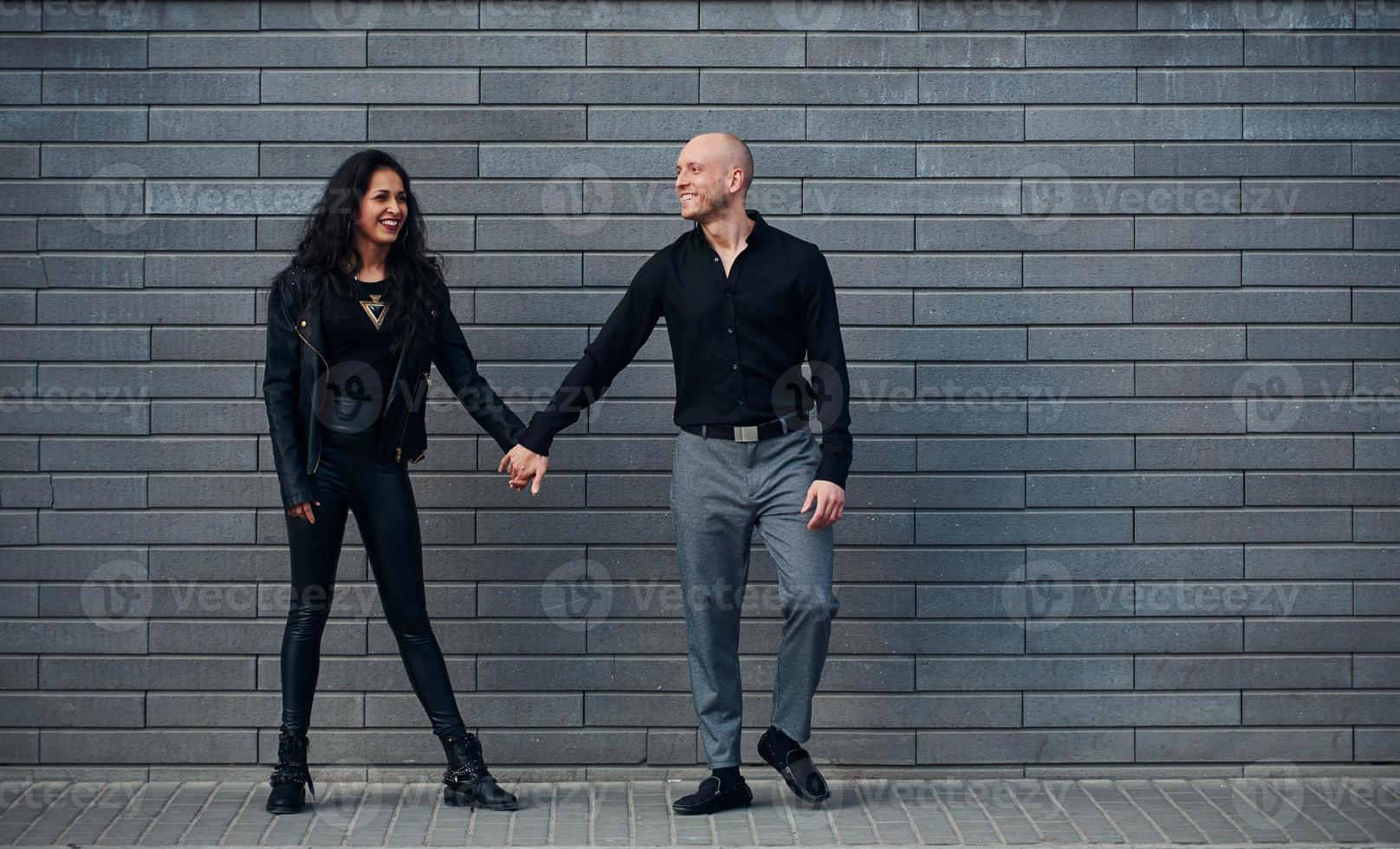 Schönes Paar in schwarzer Kleidung zusammen gegen die Wand im Freien foto