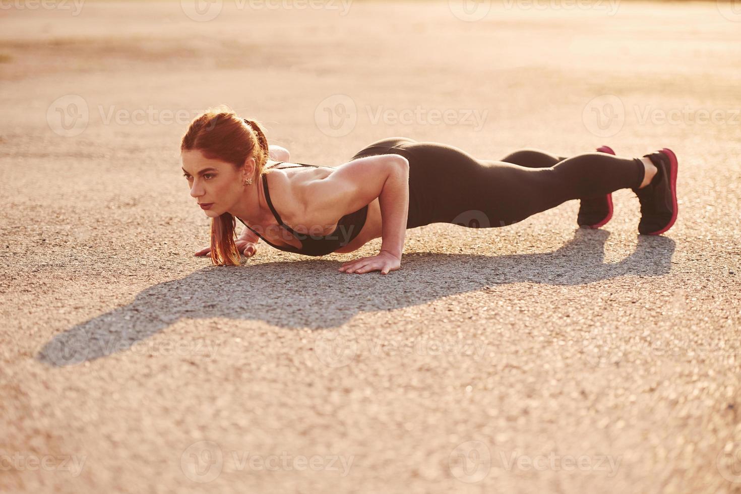 Frau in Sportbekleidung, die abends auf der Straße Liegestütze macht foto