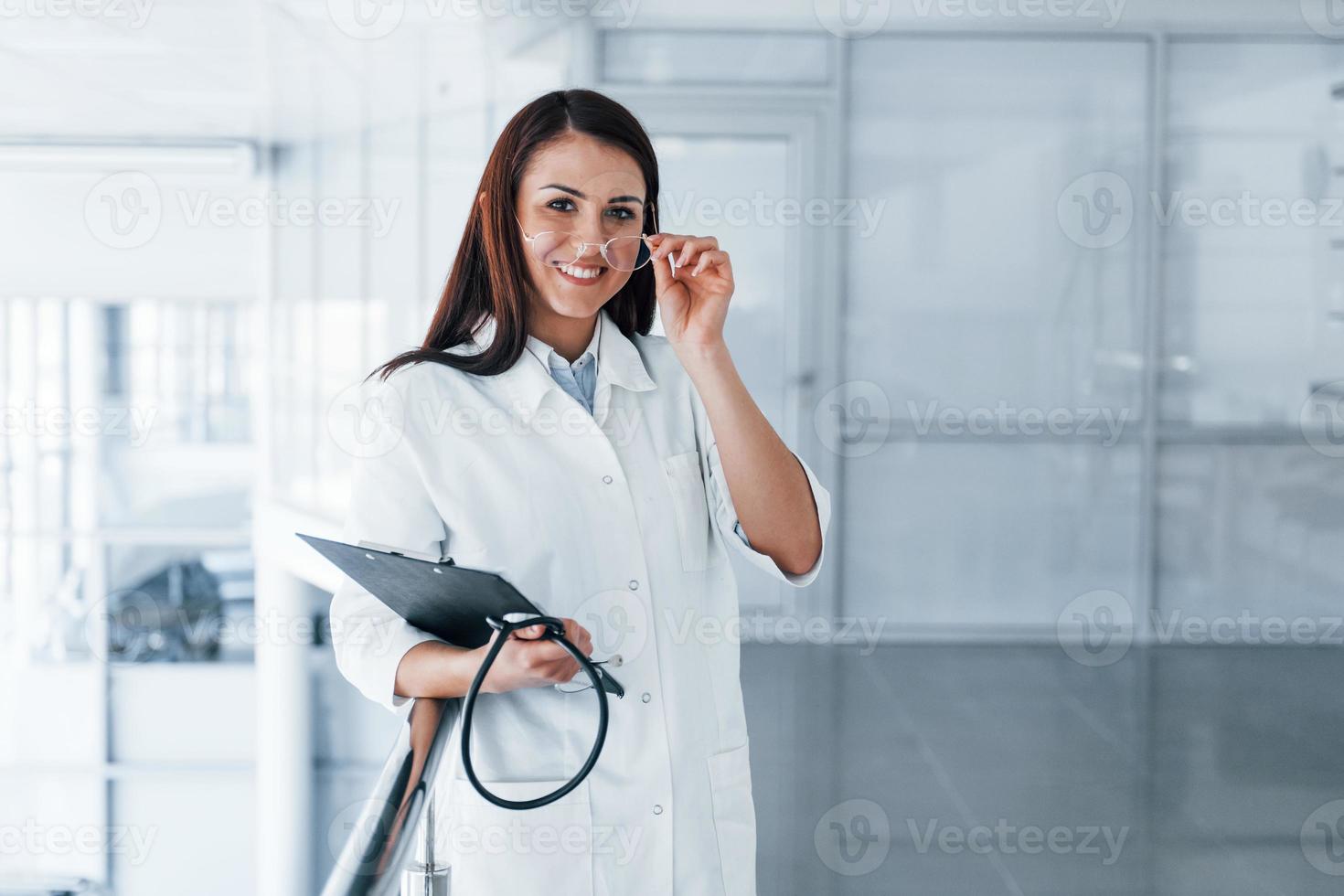 Freundliche junge Krankenschwester drinnen in einer modernen Klinik, die bereit ist, Ihnen zu helfen foto