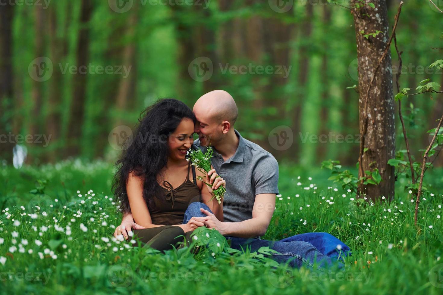 glückliches paar, das tagsüber zusammen im wald auf dem gras sitzt foto