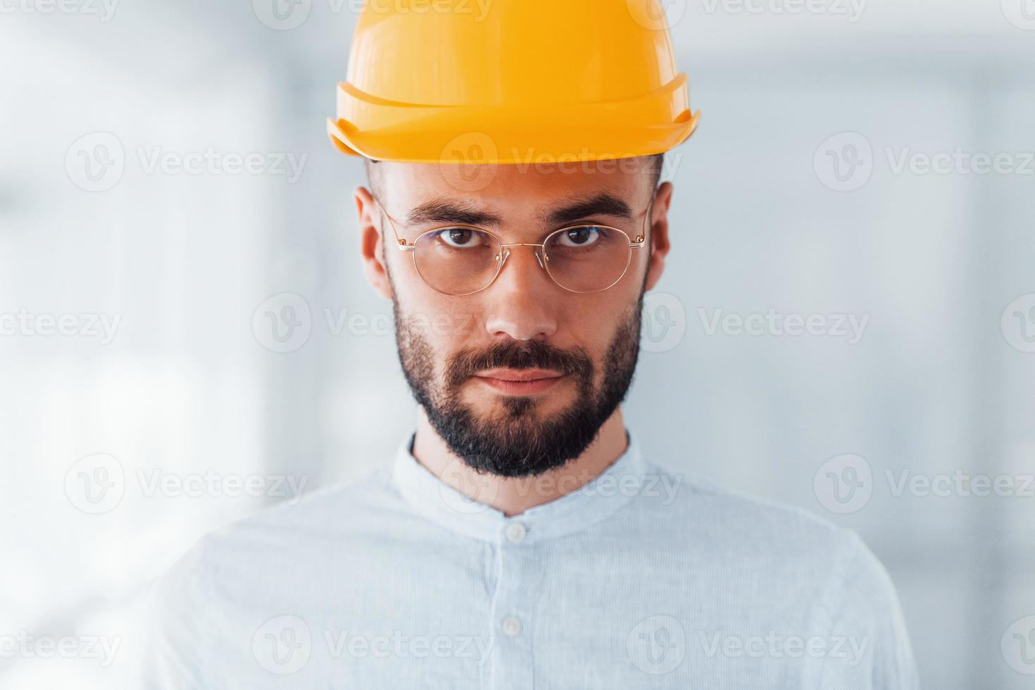 Porträt des Ingenieurs mit orangefarbenem Schutzhelm und Brille, der drinnen steht und arbeitet foto