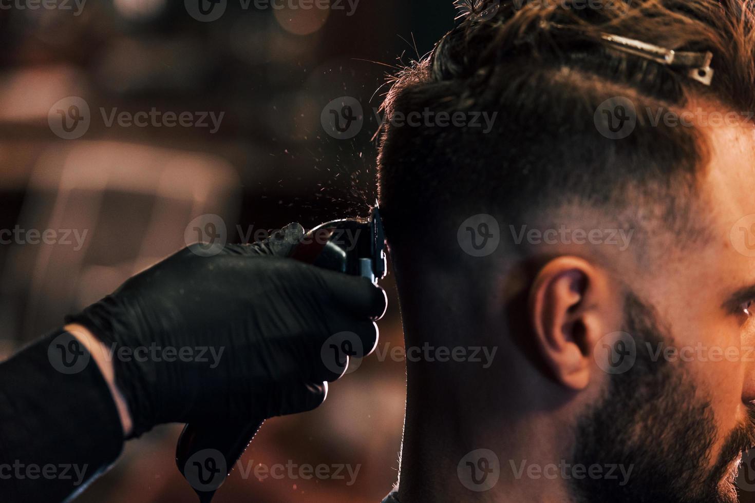 Nahaufnahme eines jungen bärtigen Mannes, der im Friseursalon sitzt und sich die Haare schneiden lässt foto