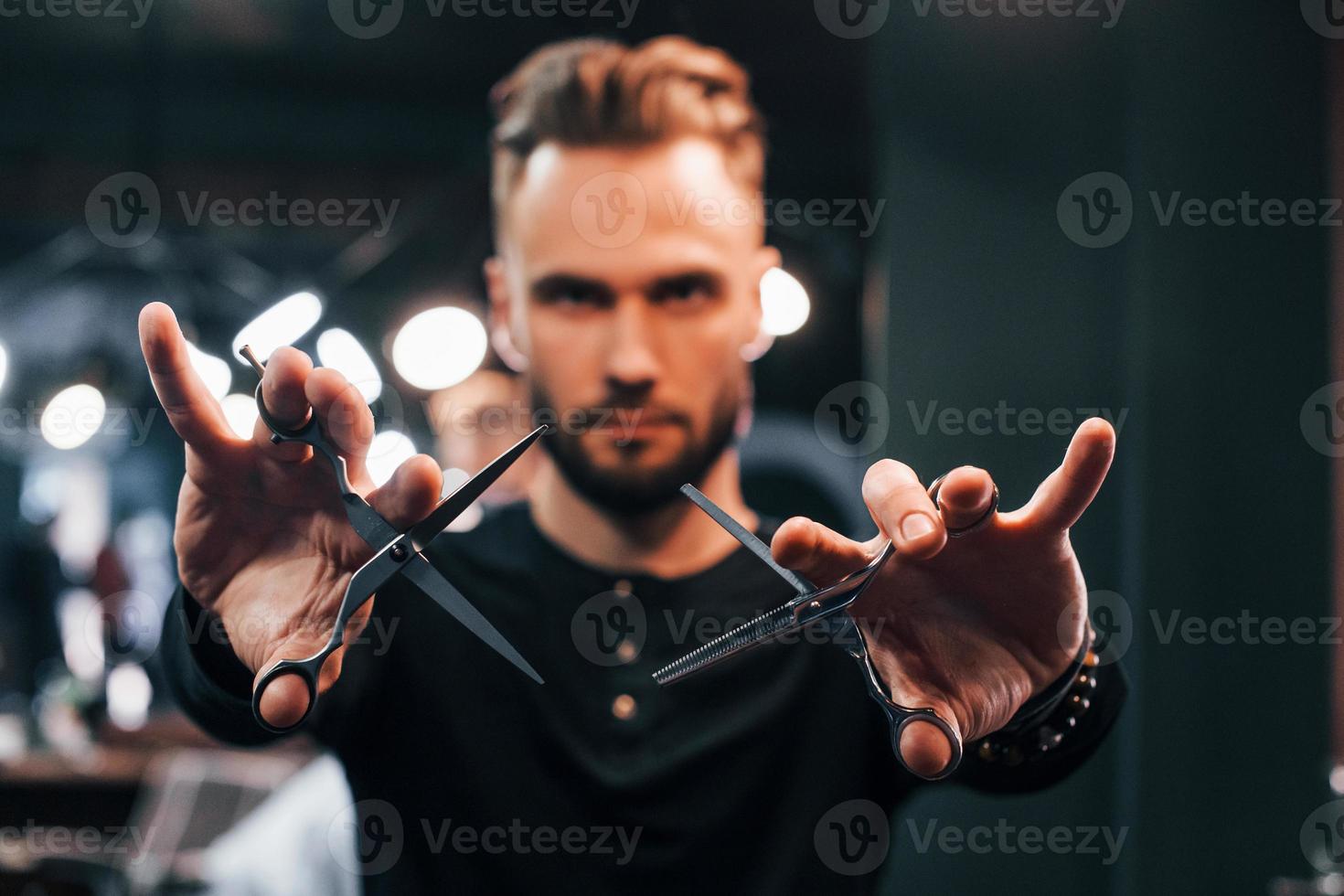 Junger bärtiger Mann, der im Friseursalon steht und eine Schere hält foto