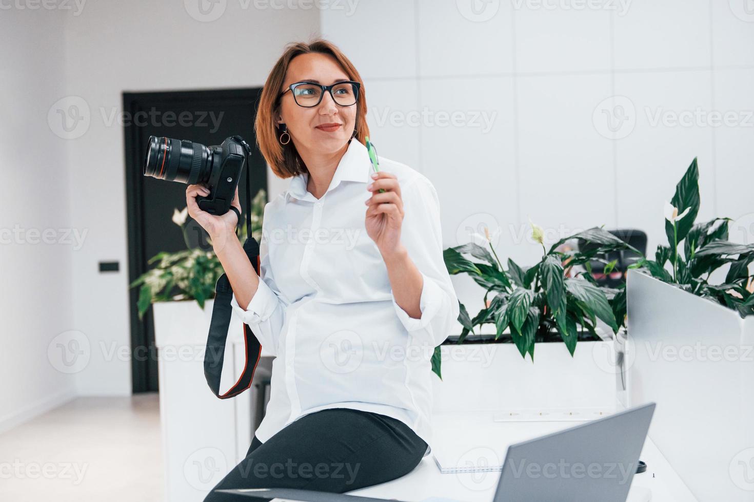 Frau in formeller Kleidung und mit Kamera im Büro foto