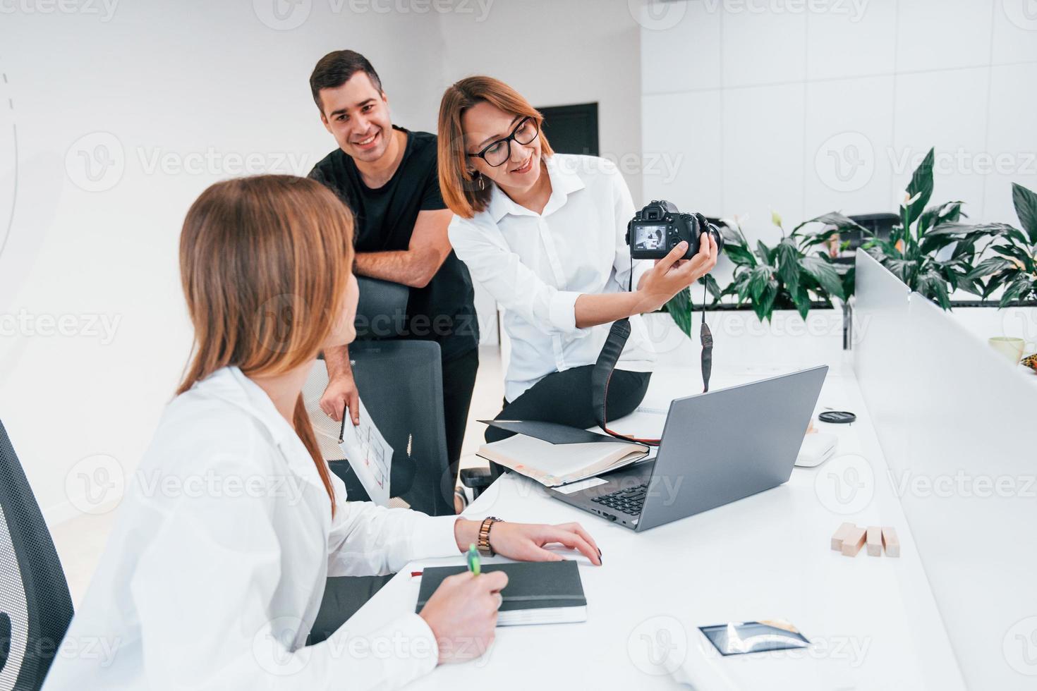 Gruppe von Geschäftsleuten in formeller Kleidung drinnen im Büro, die Fotos auf der Kamera betrachten