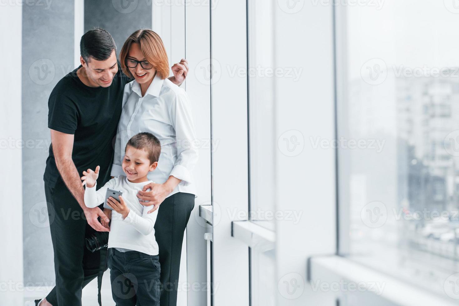 Frau in formeller Kleidung und mit Kamera in der Hand, die mit Mann und kleinem Jungen in einem leeren Raum steht foto