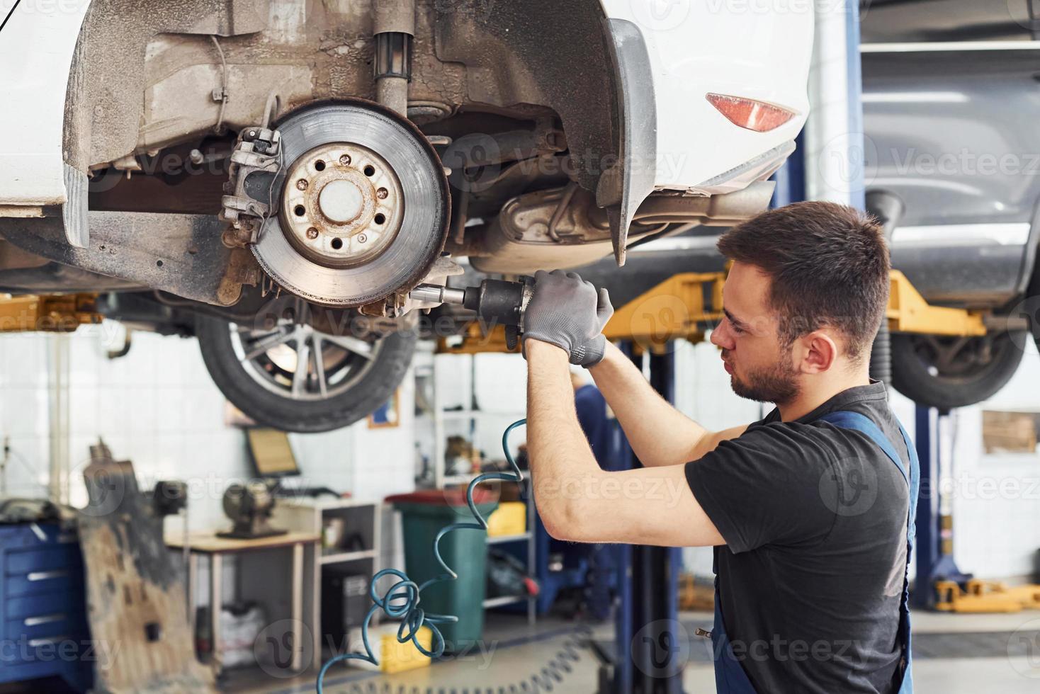 mit Spezialwerkzeug. Mann in Arbeitsuniform repariert weißes Auto drinnen.  Konzept des Autoservices 15293609 Stock-Photo bei Vecteezy