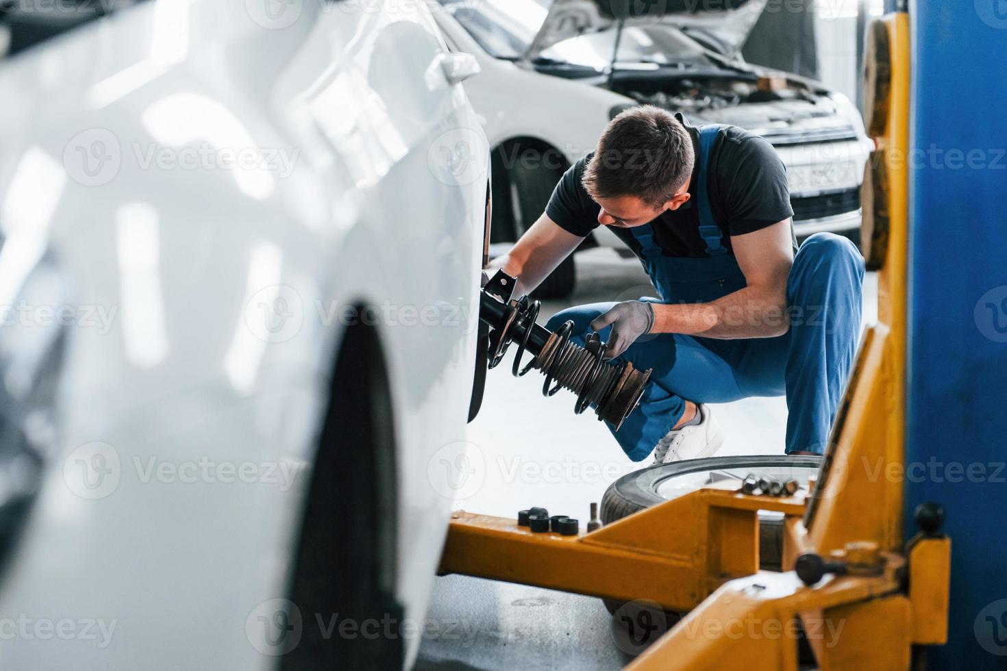 mit Spezialwerkzeug. Mann in Arbeitsuniform repariert weißes Auto drinnen.  Konzept des Autoservices 15293609 Stock-Photo bei Vecteezy