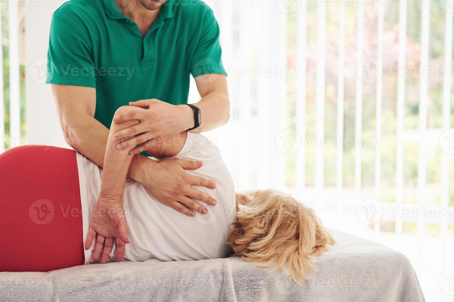 ältere frau hat einen besuch in der klinik, legt sich hin und hat rehabilitierung. männlicher lehrer hilft ihr foto