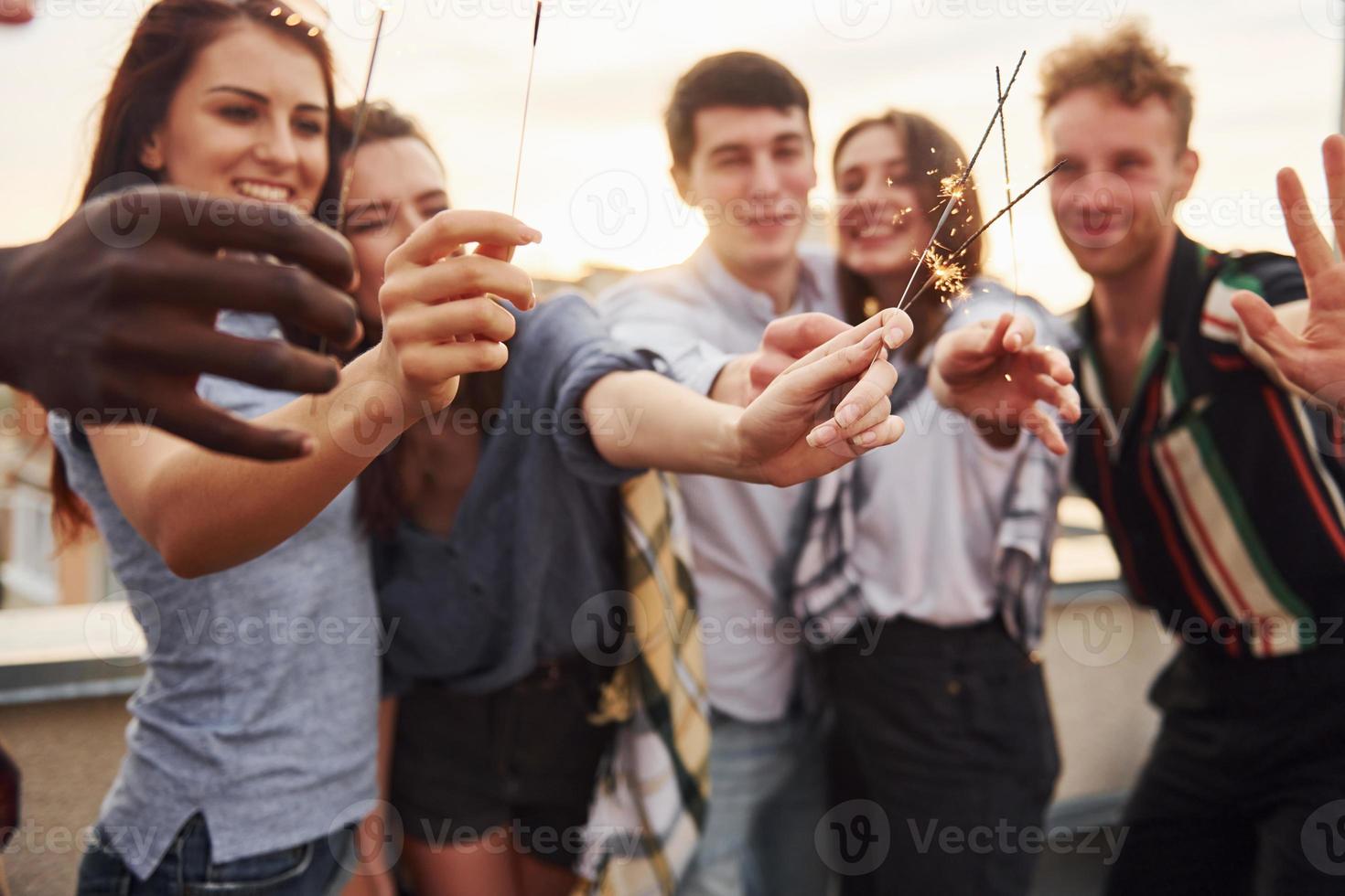 mit Wunderkerzen in den Händen. eine gruppe junger leute in lässiger kleidung feiert tagsüber zusammen eine party auf dem dach foto