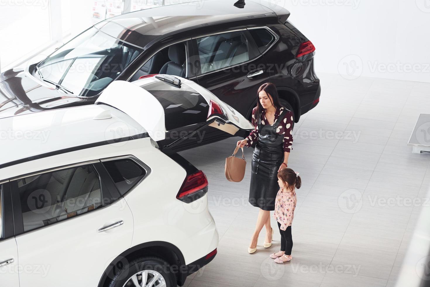 mutter mit ihrer tochter, die zusammen in der nähe eines modernen autos drinnen spazieren geht foto