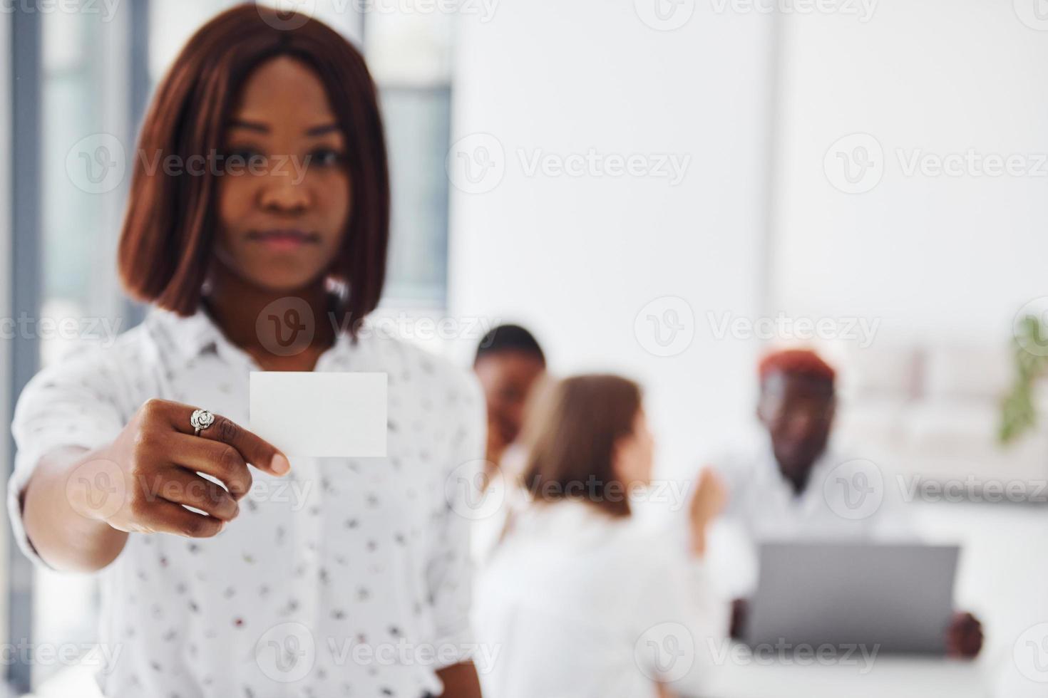 Frau hält Visitenkartenkarte. gruppe von afroamerikanern, die gemeinsam im büro arbeiten foto