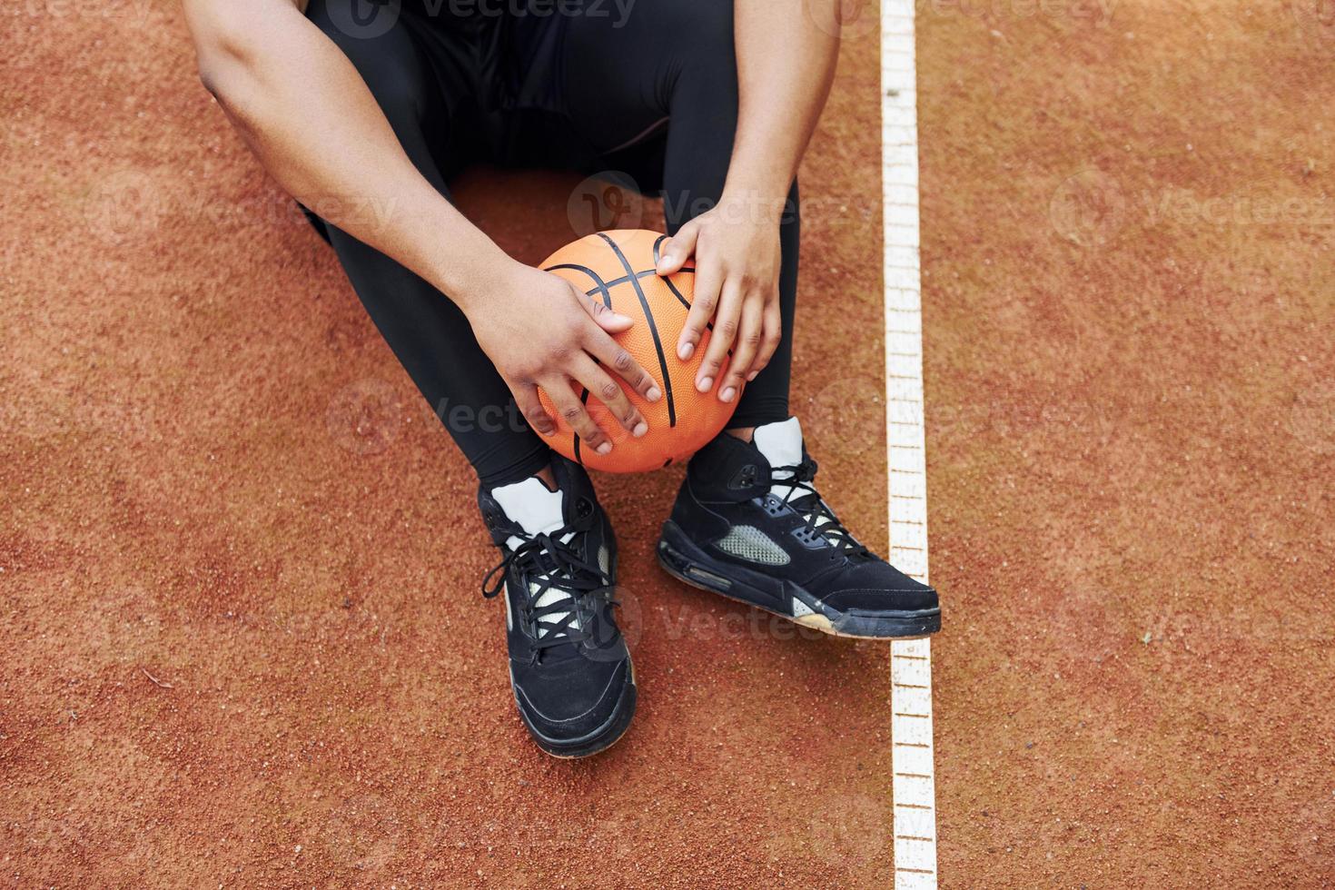 müder afroamerikaner sitzt mit ball auf dem platz im freien auf dem boden. macht eine Pause foto