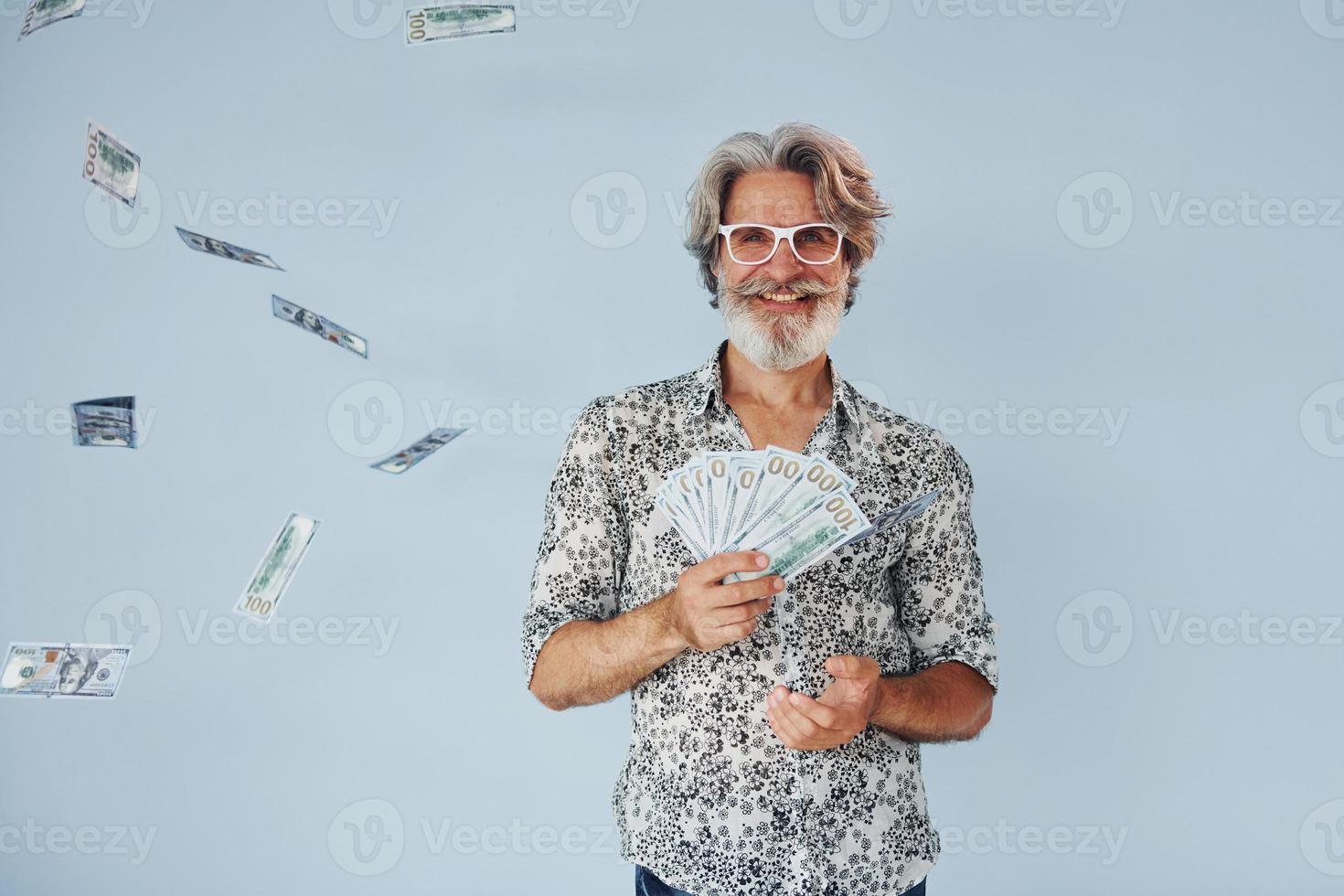 Millionär mit Bargeld in den Händen. Senior stilvoller moderner Mann mit grauem Haar und Bart drinnen foto