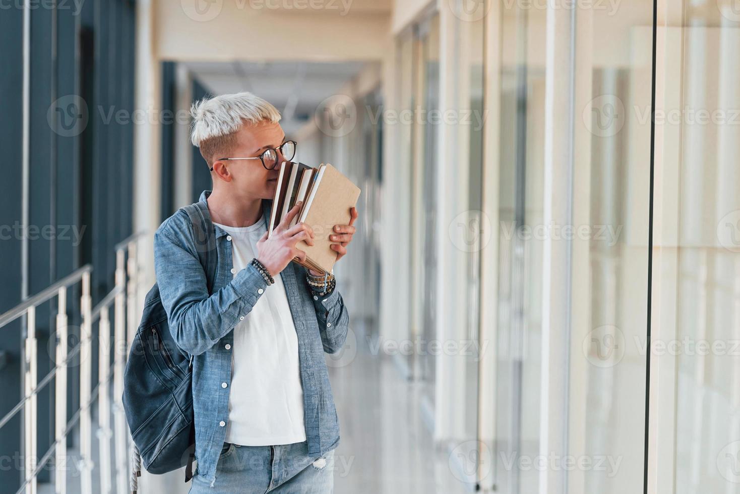 männlicher junger student in jeanskleidung ist im flur eines colleges mit büchern in den händen foto