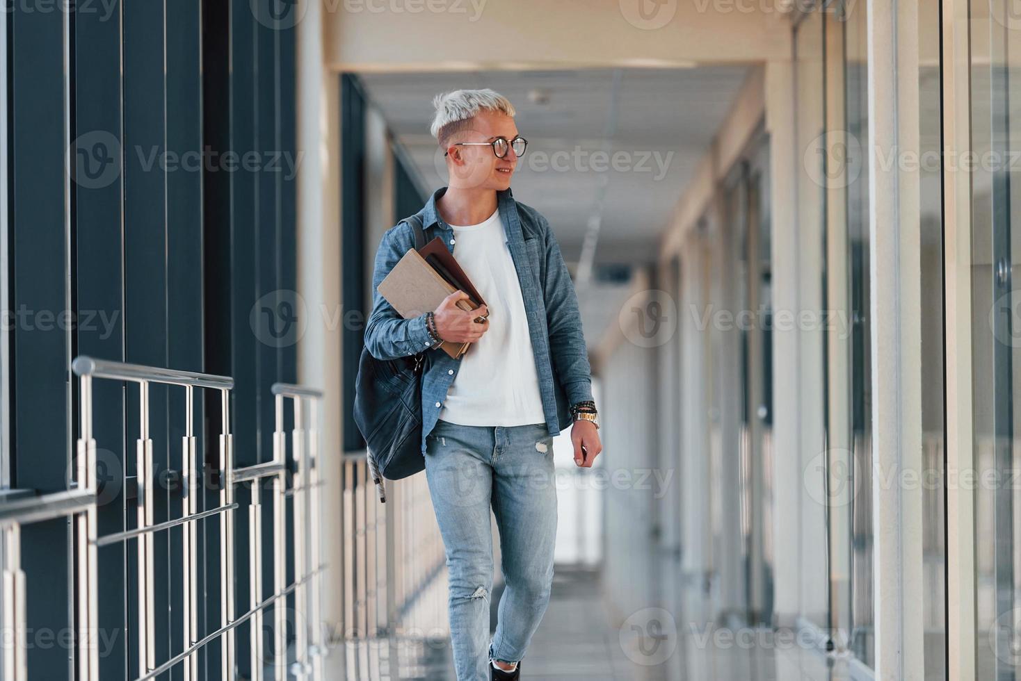 männlicher junger student in jeanskleidung ist im flur eines colleges mit büchern in den händen foto