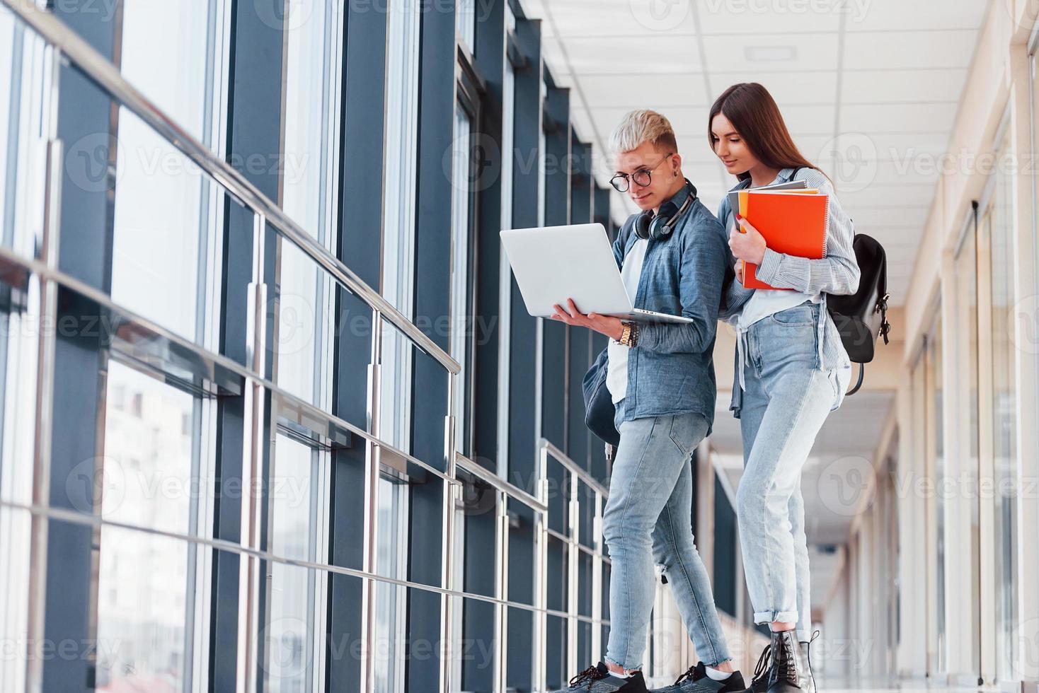 Zwei junge Studentenfreunde zusammen in einem Korridor eines Colleges mit Laptop in den Händen foto