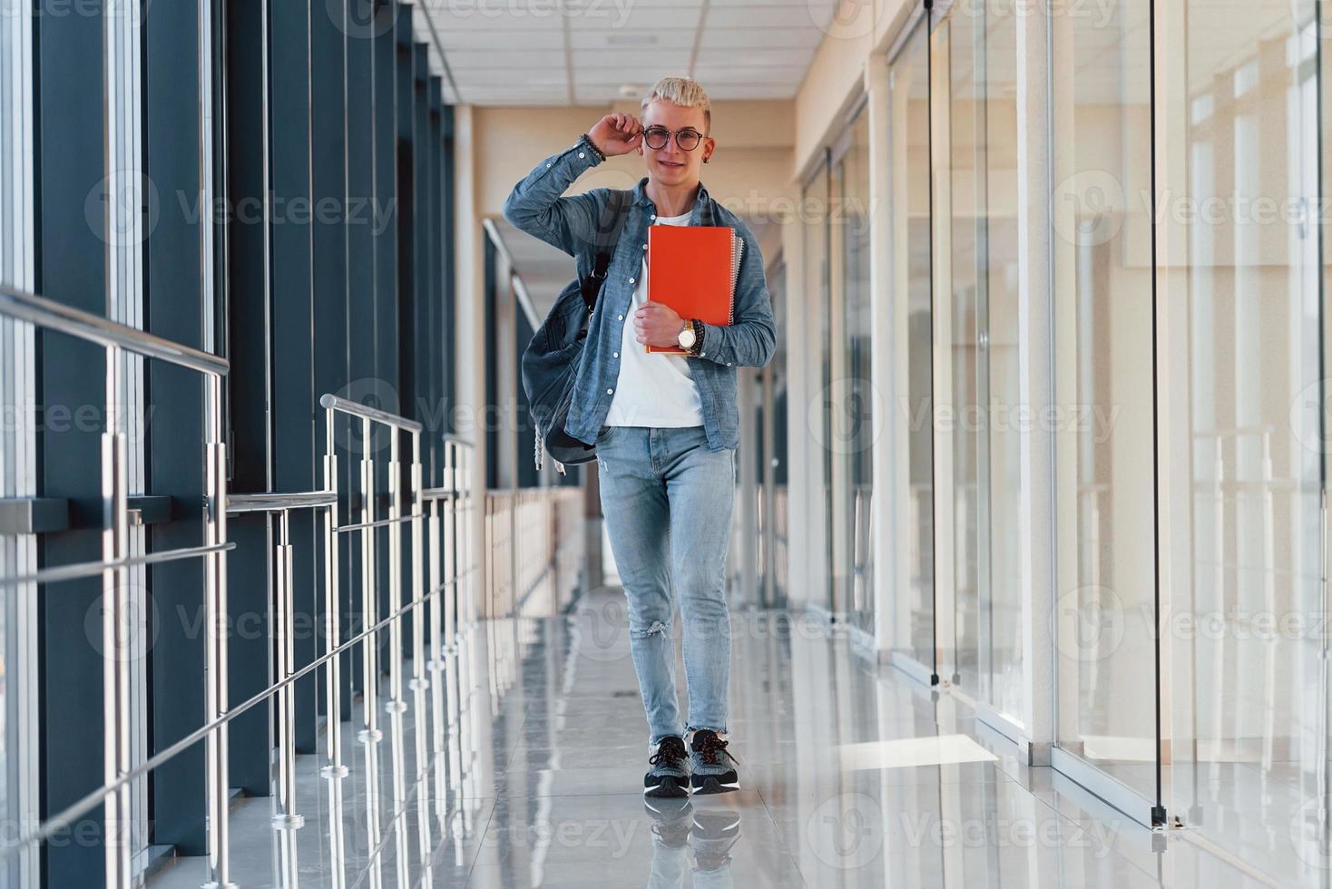 männlicher junger student in jeanskleidung ist im flur eines colleges mit notizblock in den händen foto